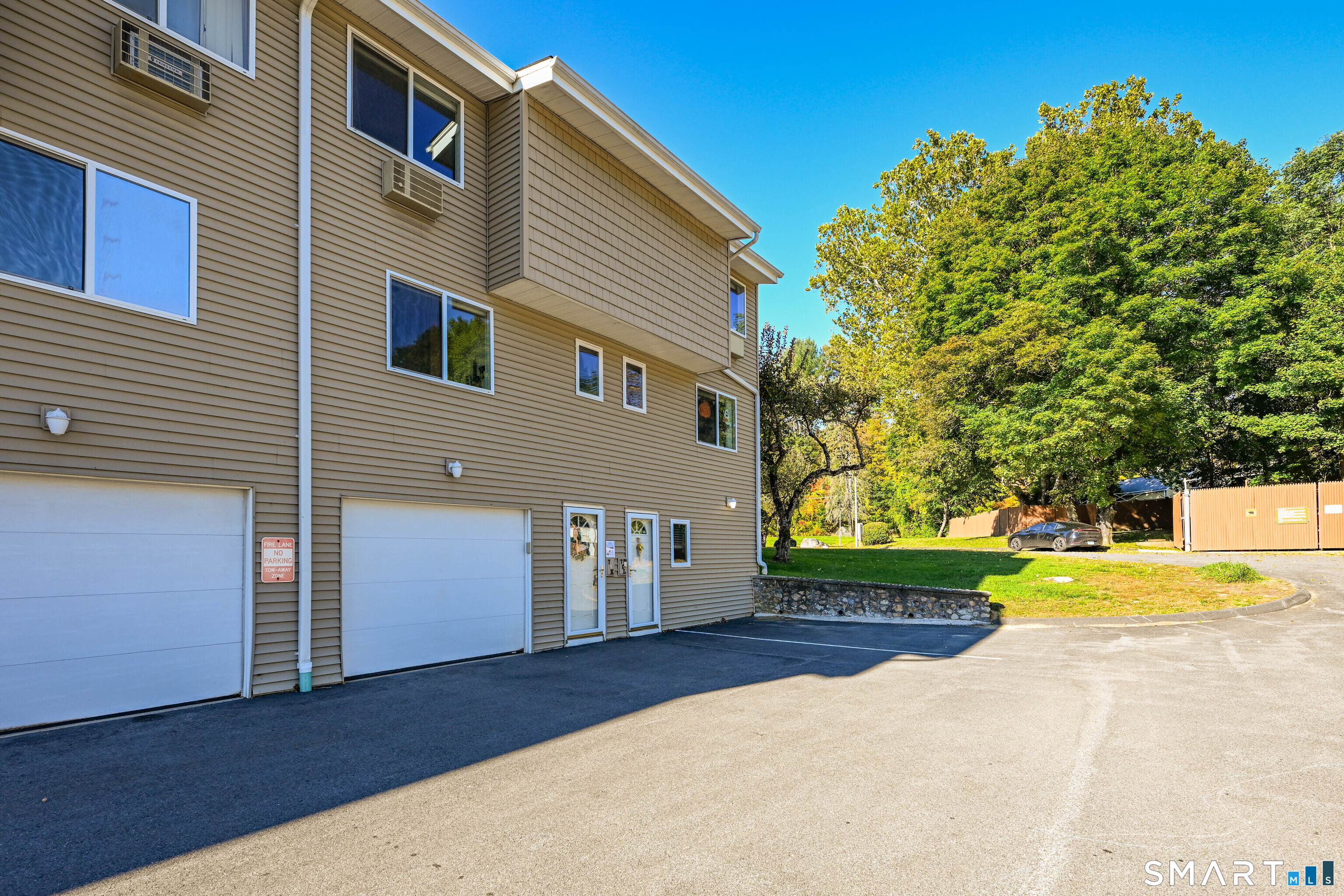 Multi-unit building with tan siding, garage doors, and a paved parking area.