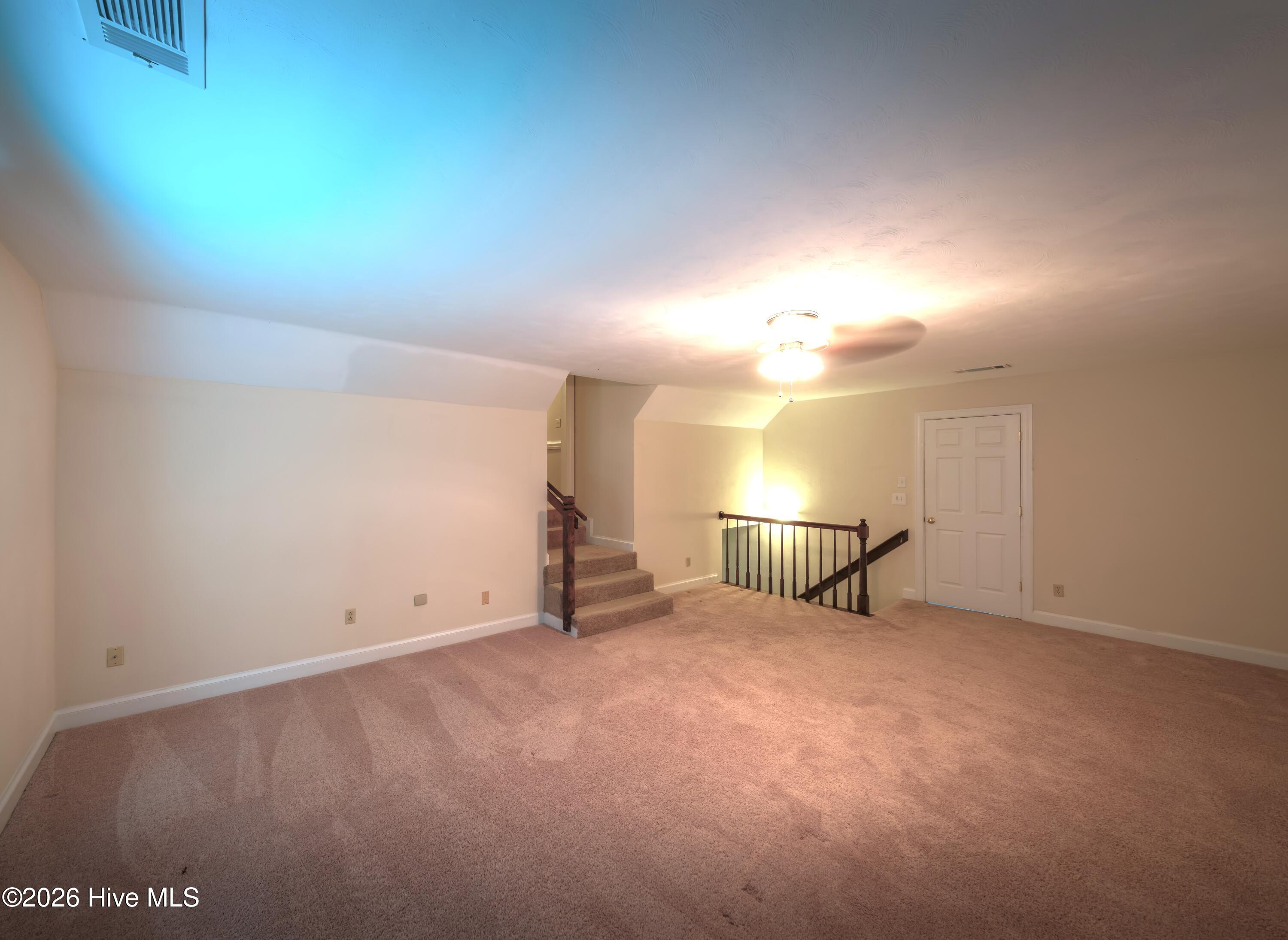 Vacant carpeted room with steps and a railing surrounding the stairwell.