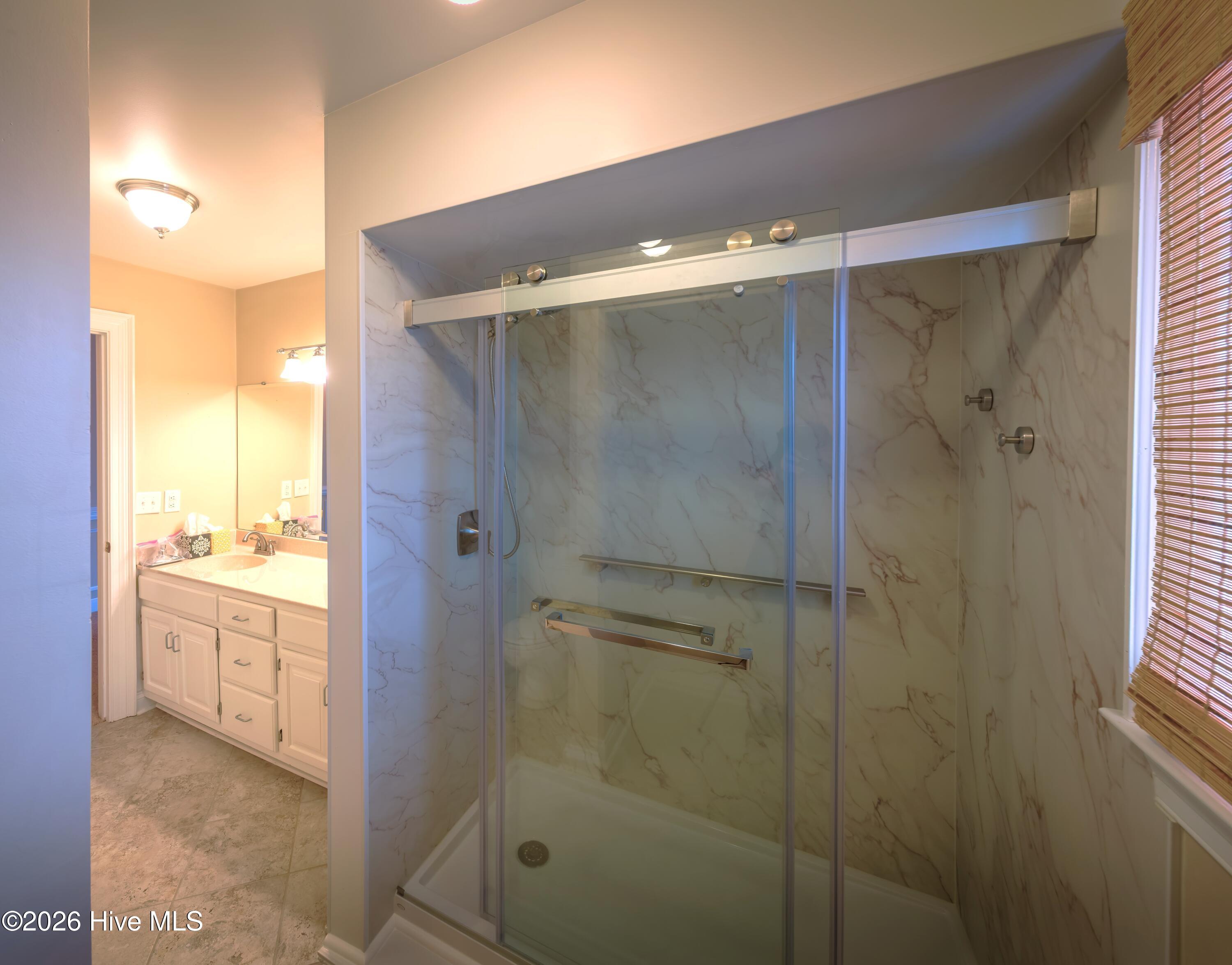 Bathroom with glass-enclosed shower, marble-look walls, and adjacent white vanity.