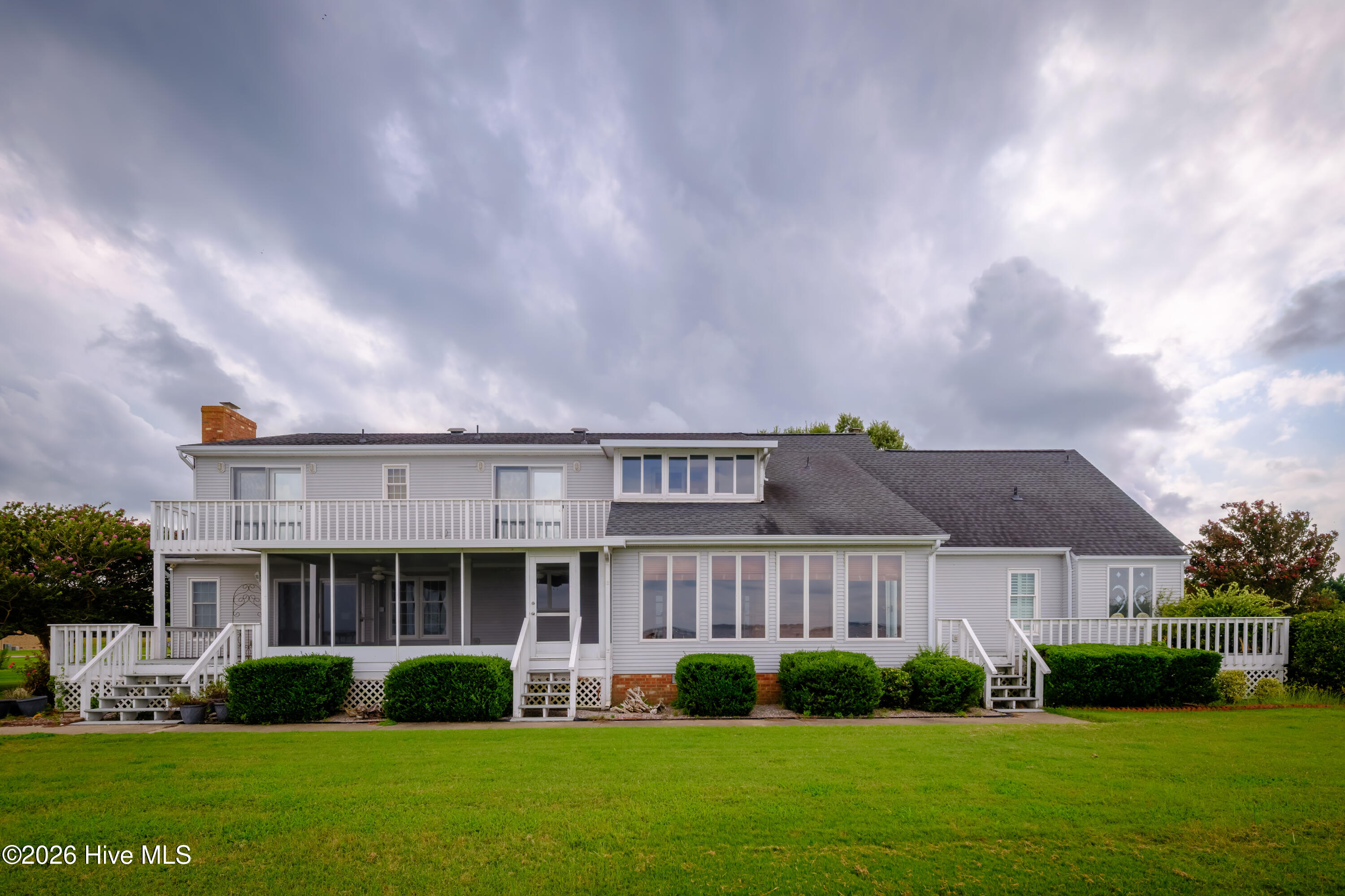 House rear with white-railed decks, a screened porch, and a broad green lawn.