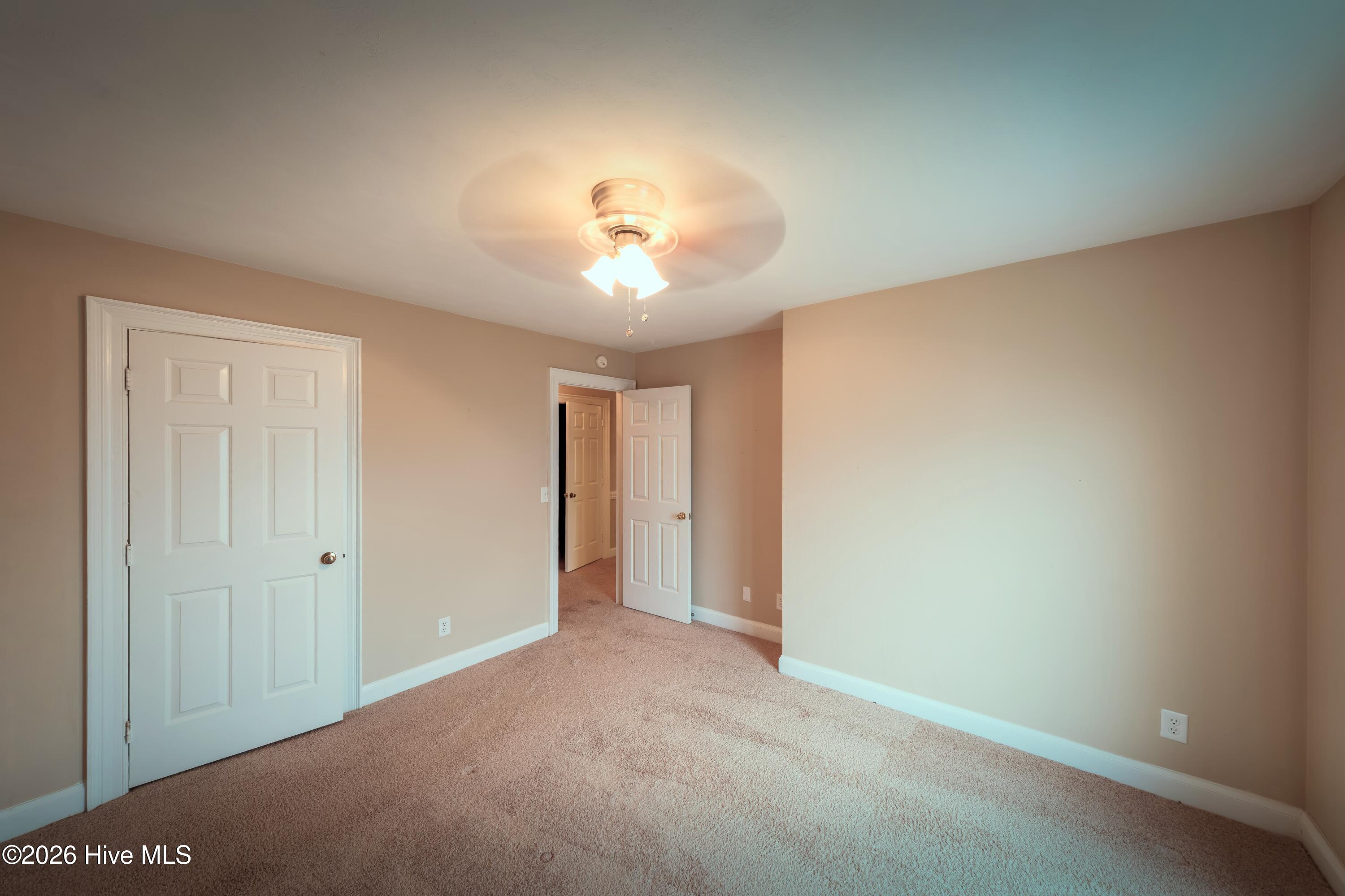 Empty carpeted bedroom with beige walls, a ceiling fan light, and two white doors.