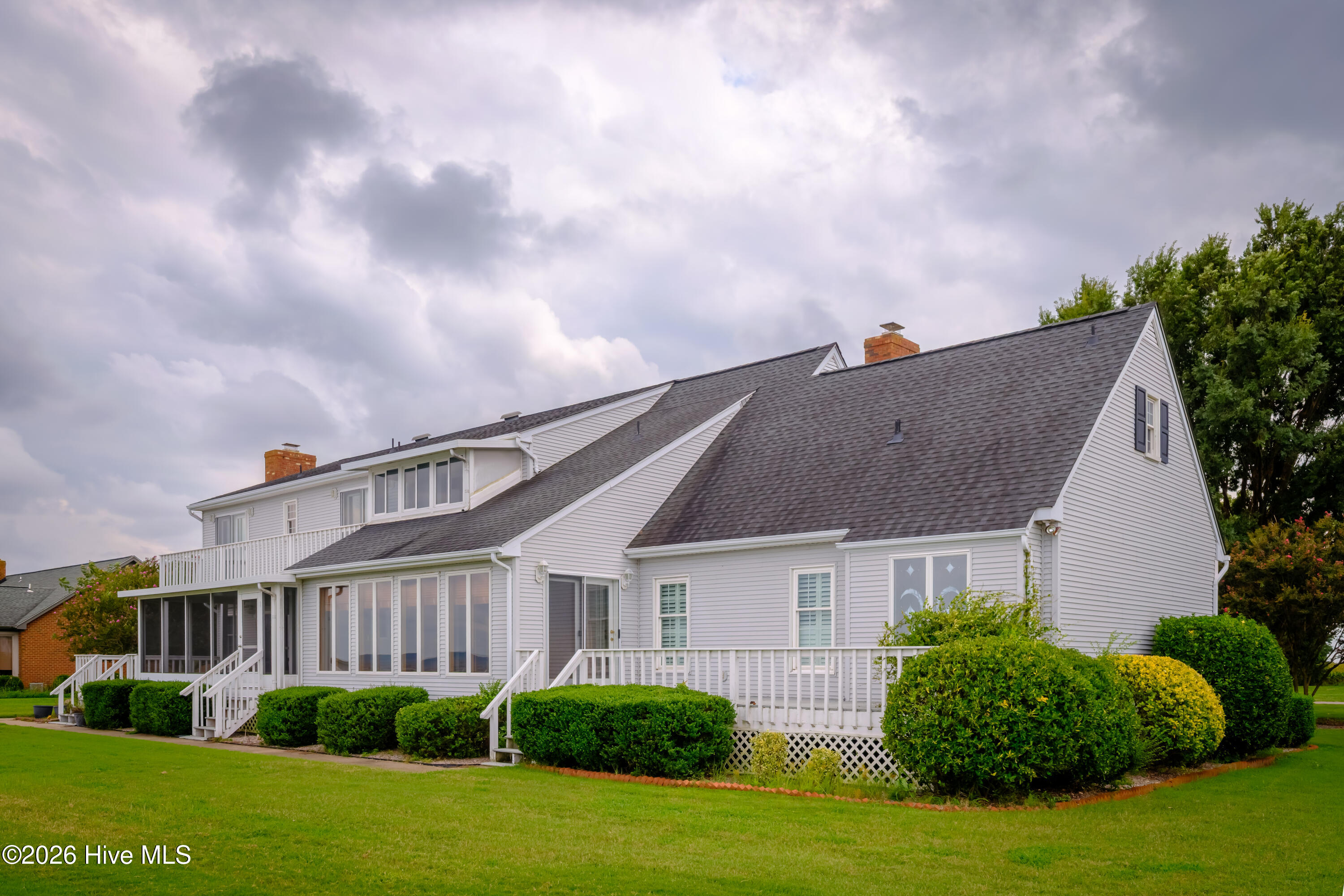 White-sided house with multiple gables, a screened porch, white decks, and a broad green lawn.