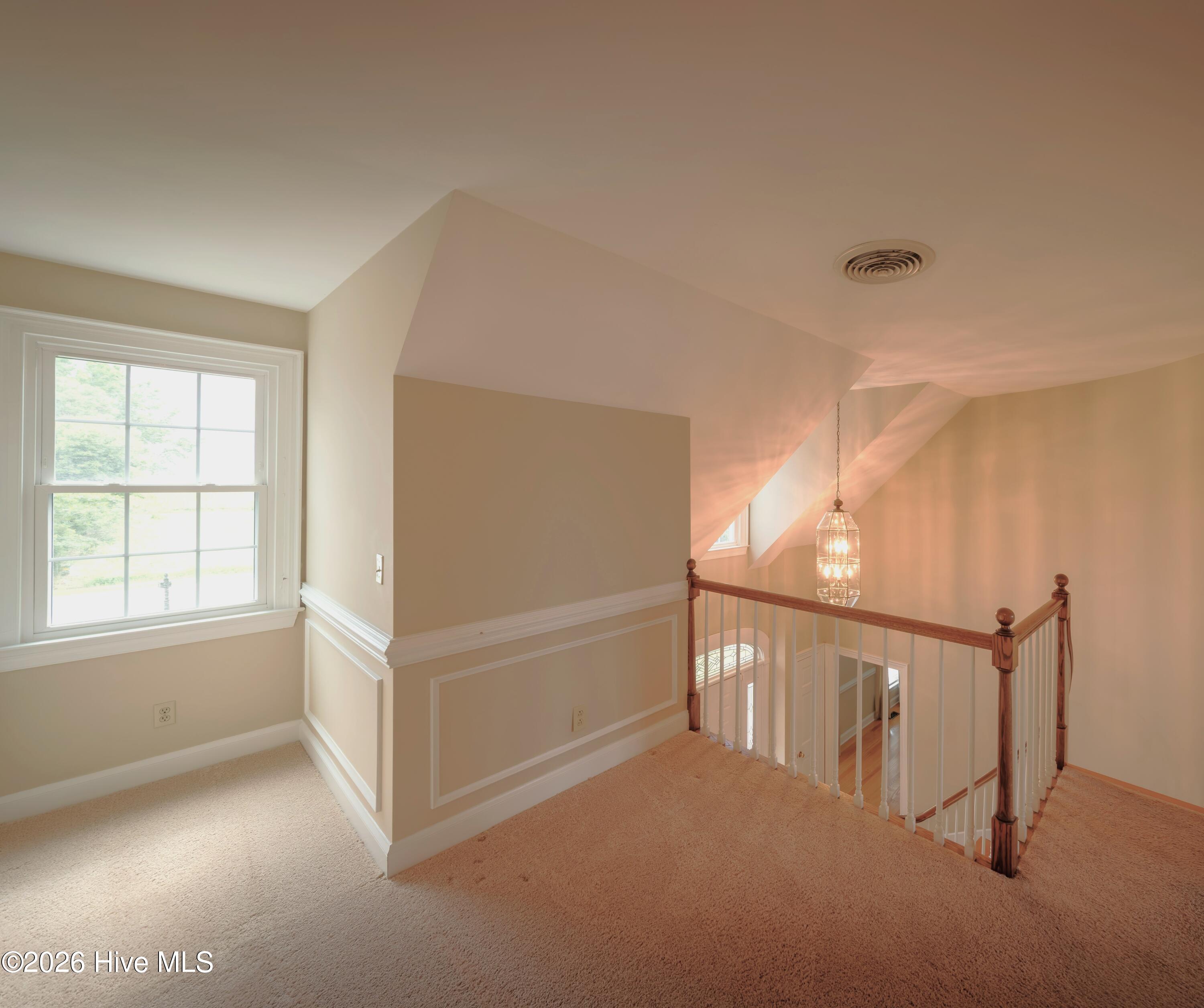 Upstairs landing with beige carpet, a large window, and a wood-and-white stair railing beside a hanging lantern.