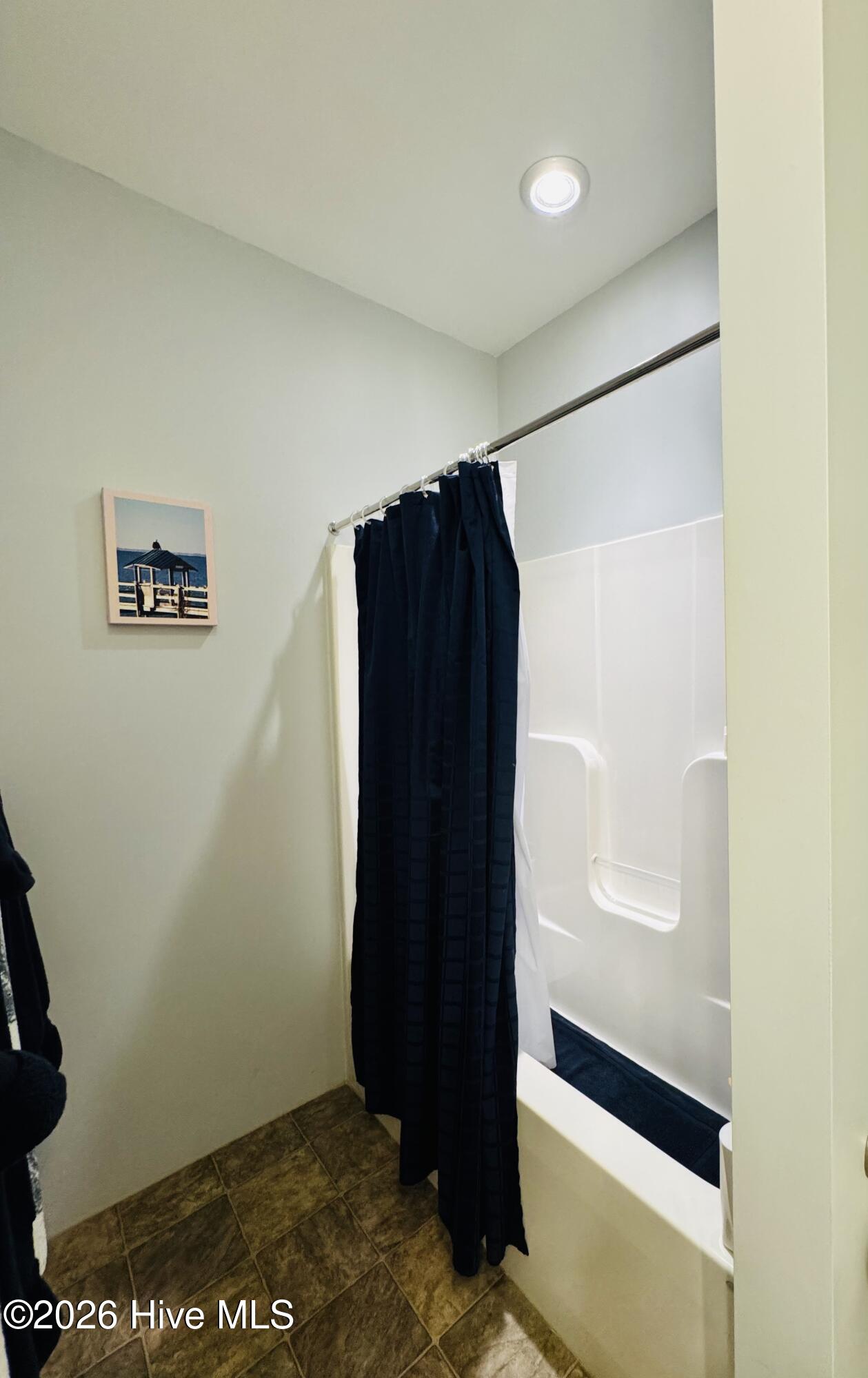 Bathroom with a white tub and shower, navy curtain, and brown tiled floor