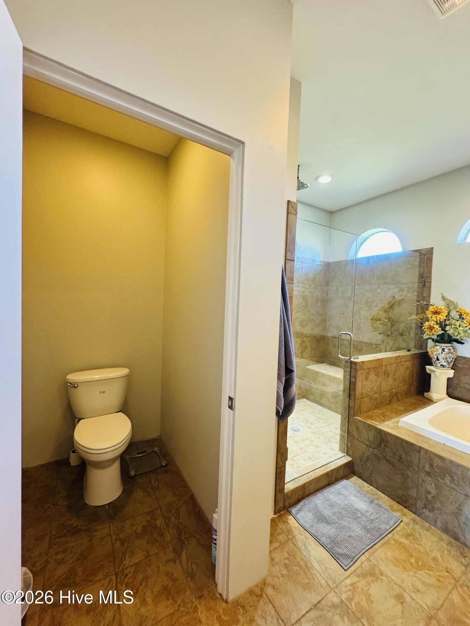 Bathroom with glass-enclosed shower, built-in soaking tub, and separate toilet closet.