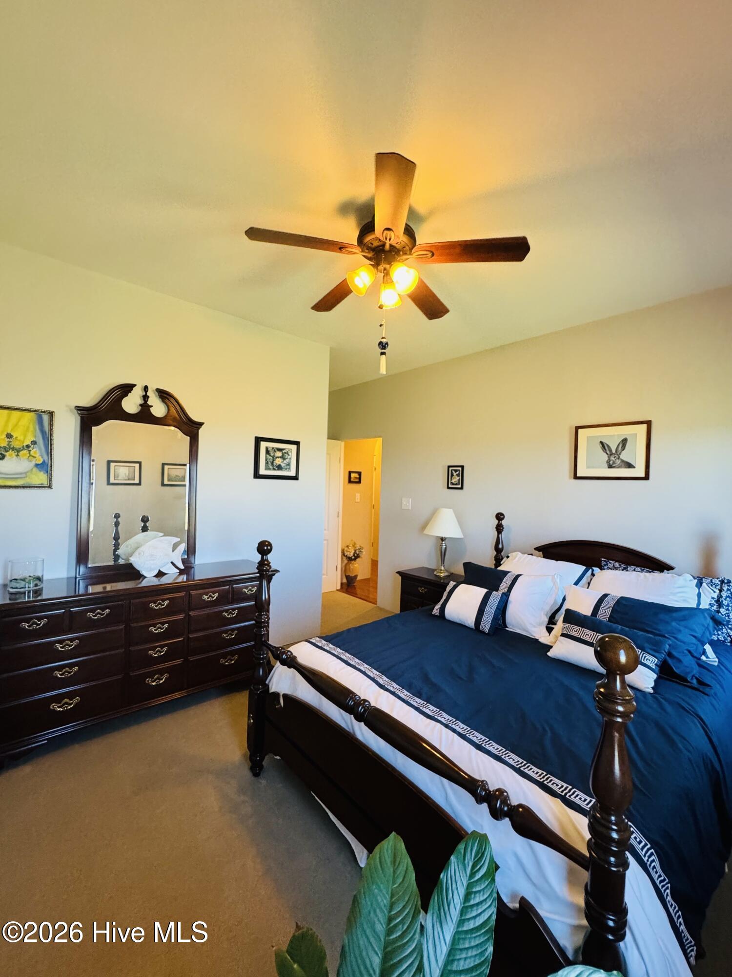 Bedroom with a dark wood four-poster bed, blue-and-white bedding, matching dresser, and lit ceiling fan.