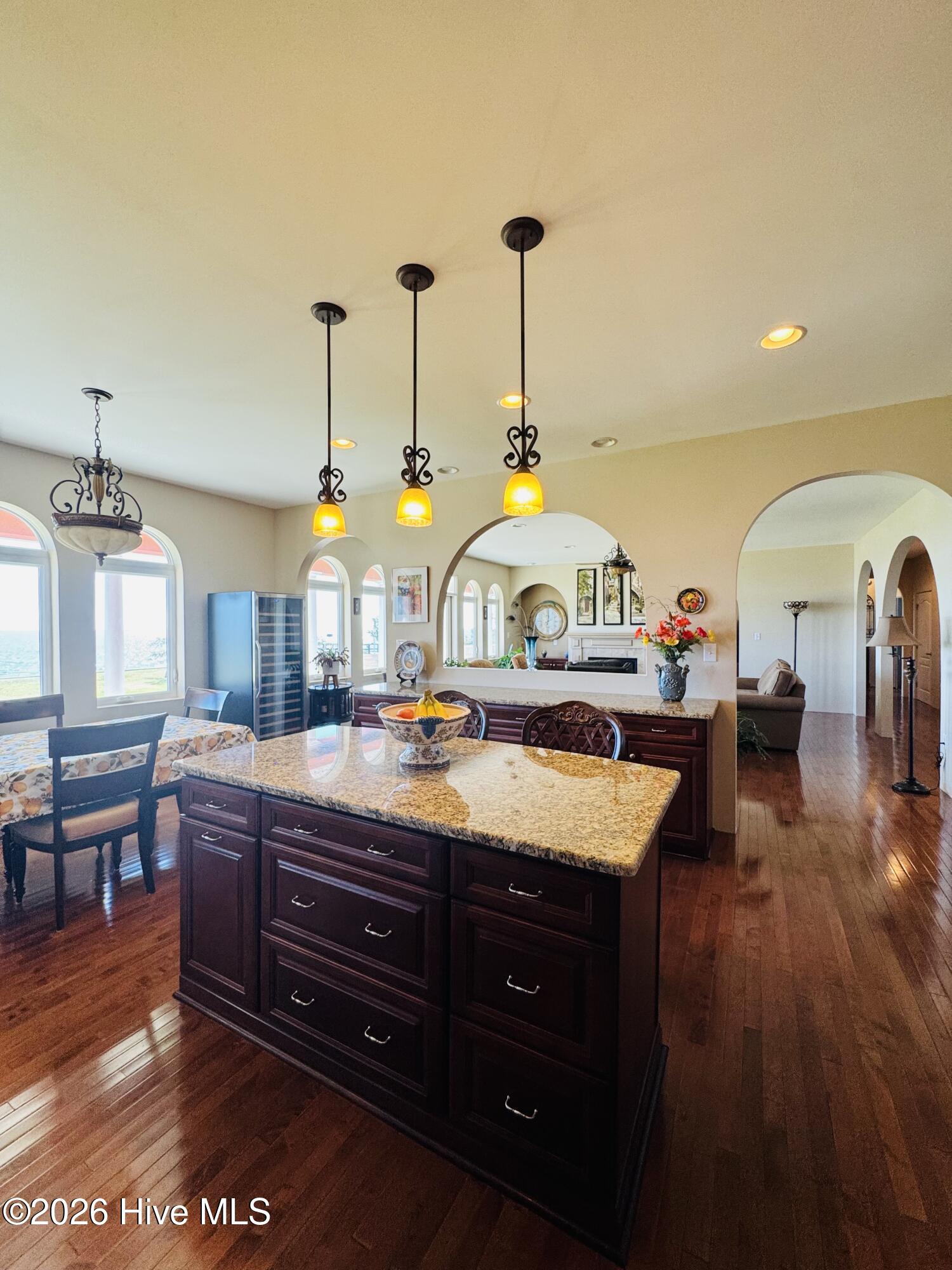 Kitchen with granite island, dark wood cabinets, pendant lights, and arched windows.