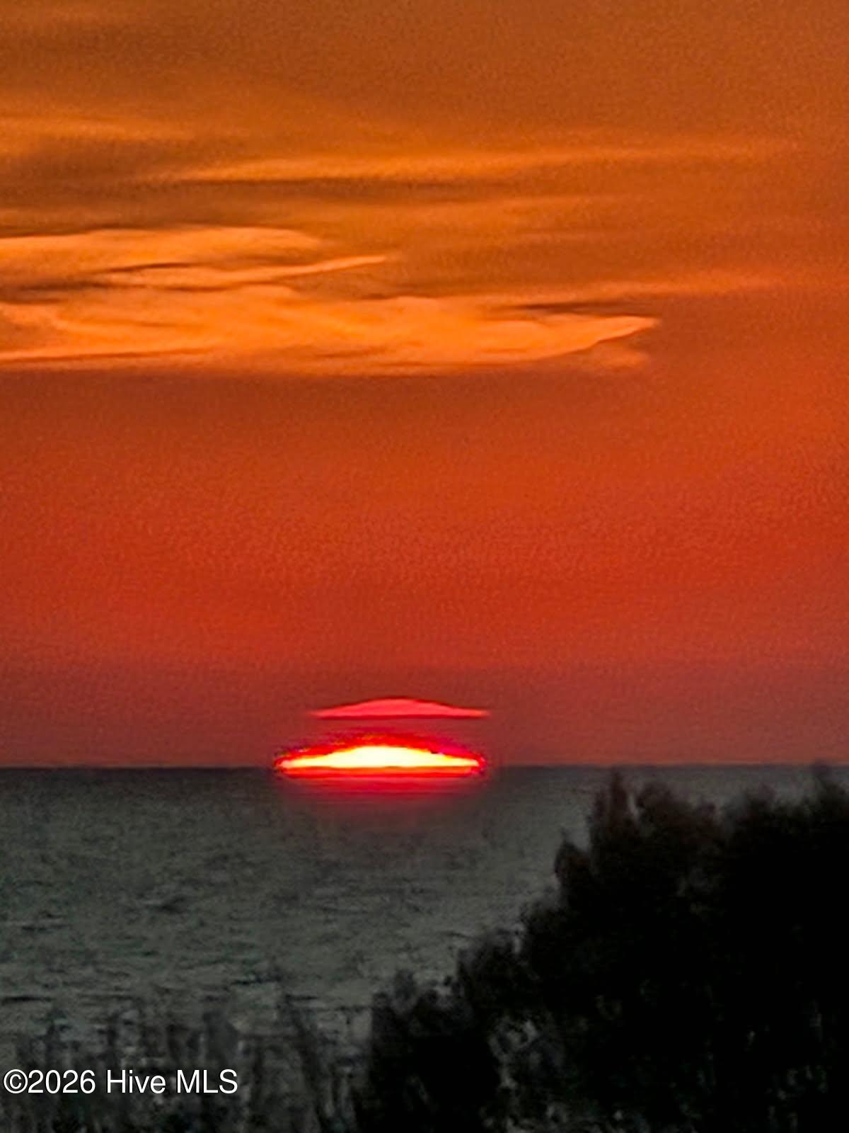 Red-orange sunset over rippling water, framed by dark shoreline vegetation.