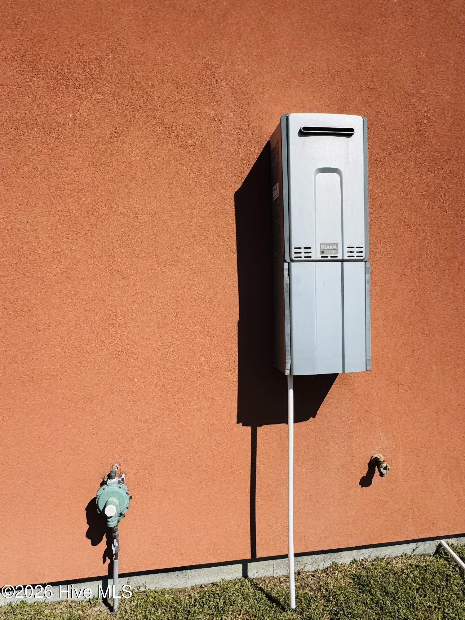 Wall-mounted tankless water heater and utility connections on an orange stucco exterior wall.
