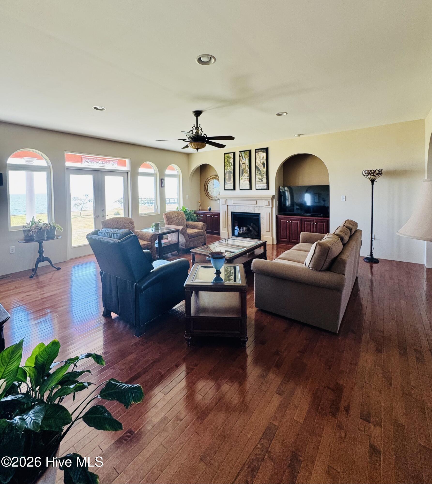Furnished living room with hardwood floors, fireplace, and large windows overlooking the water.