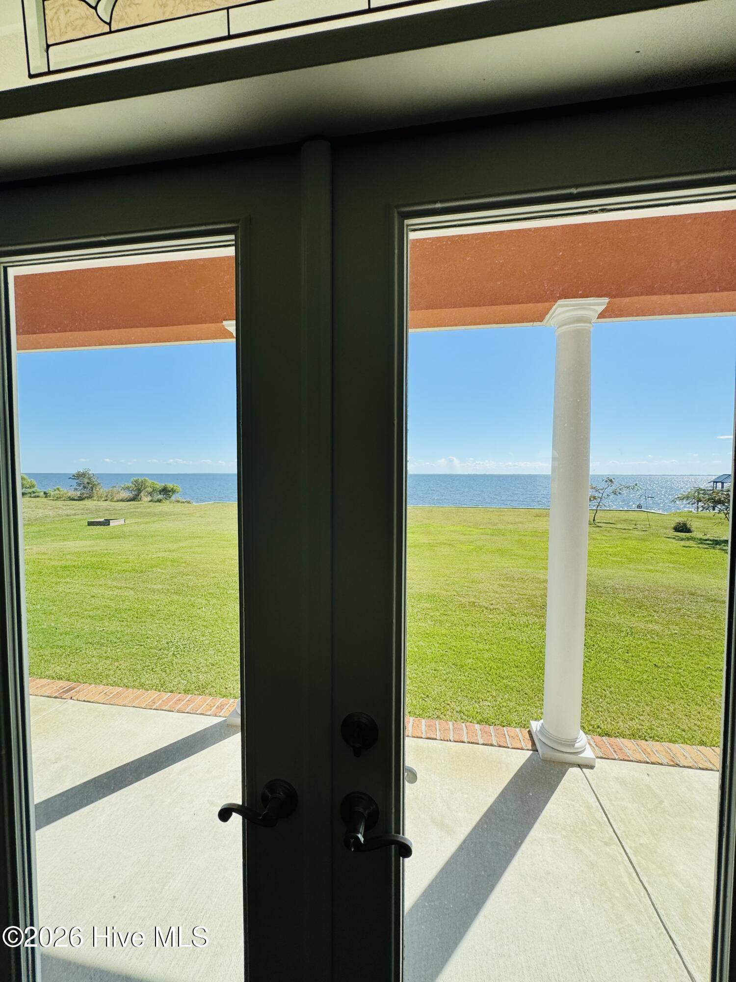 Glass doors open onto a columned patio overlooking a lawn and waterfront.