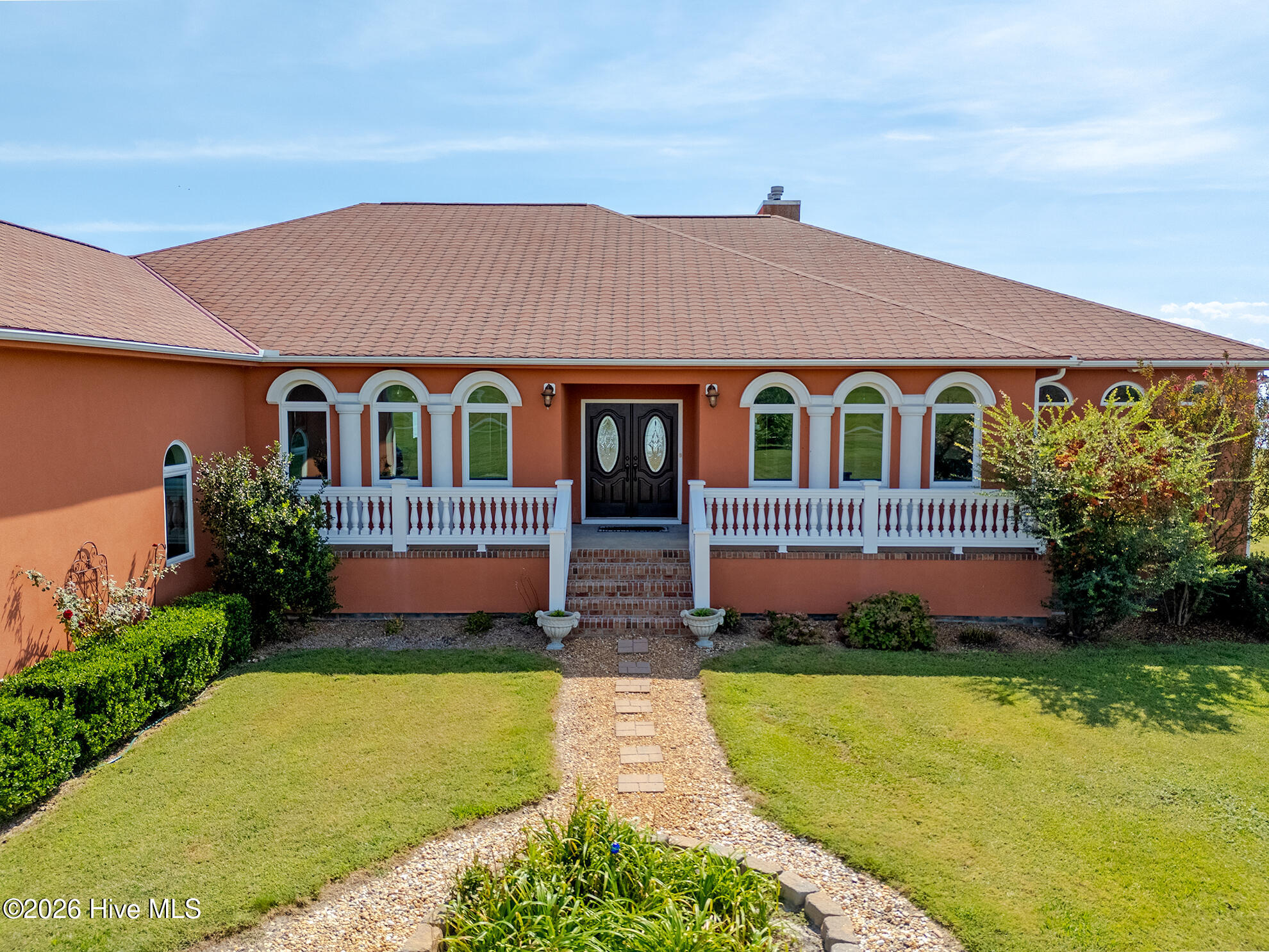 Orange stucco home with arched windows, dark double doors, and a curved gravel path through the lawn.