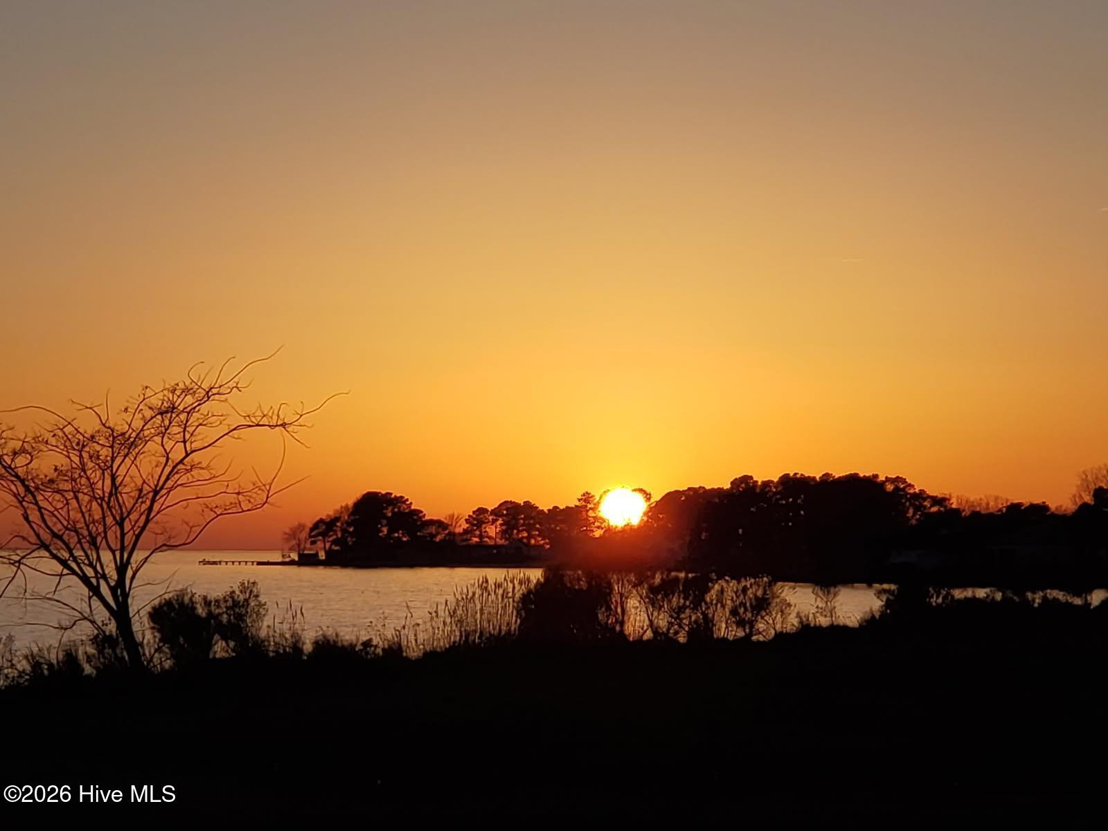 Sunset over the water with a tree-lined shore and small dock.