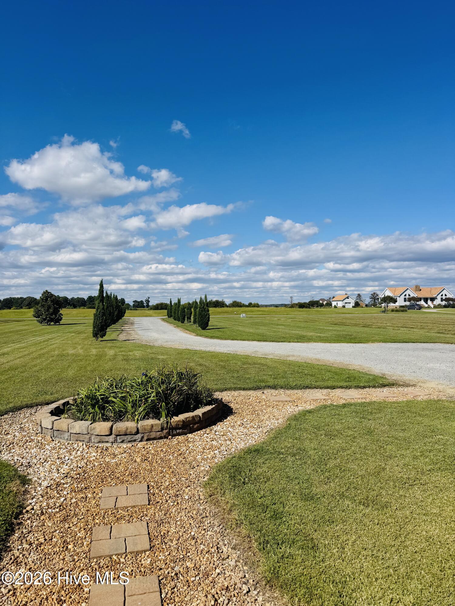 Landscaped front yard with a gravel garden, curved driveway, and distant white house.