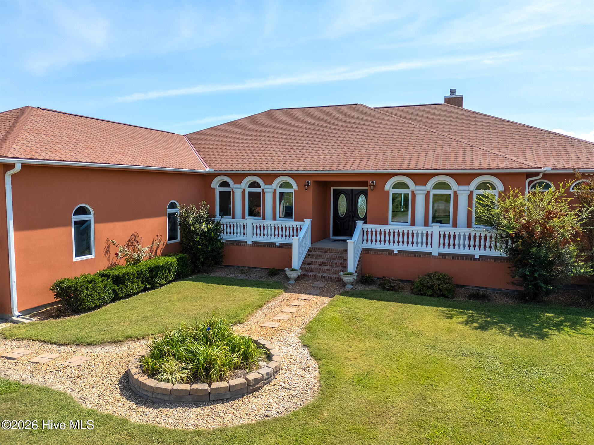 Orange stucco home with arched windows, white entry railings, and a landscaped front lawn.