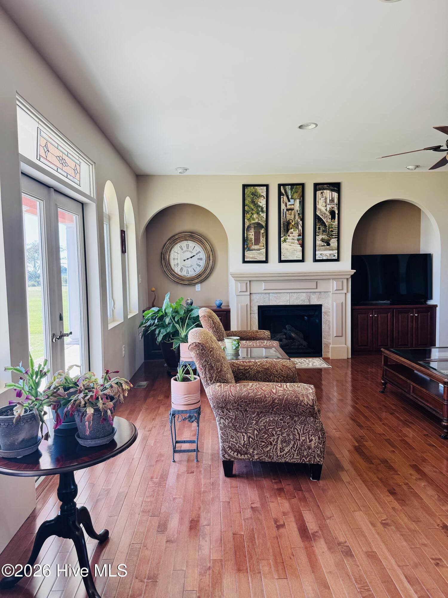 Living room with a fireplace, hardwood floors, patterned armchairs, and tall windows.