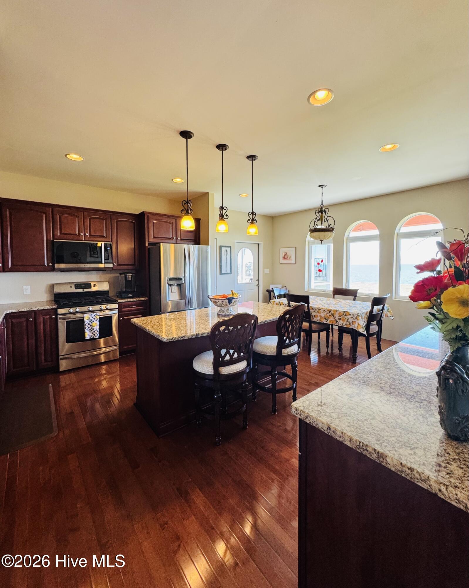 Kitchen and dining area with a granite island and arched windows overlooking the water.
