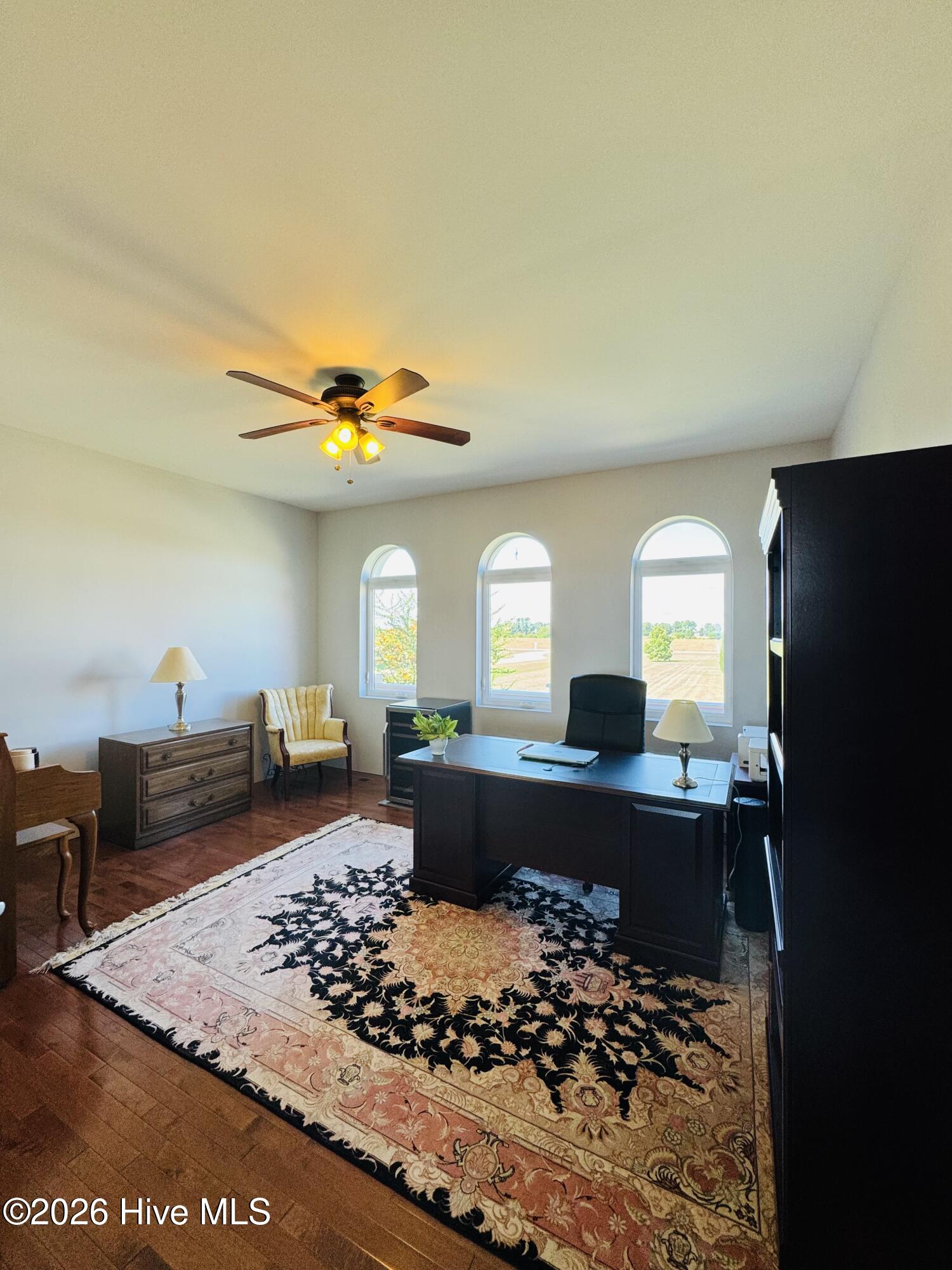 Furnished home office with a dark desk, three arched windows, and an ornate patterned rug.