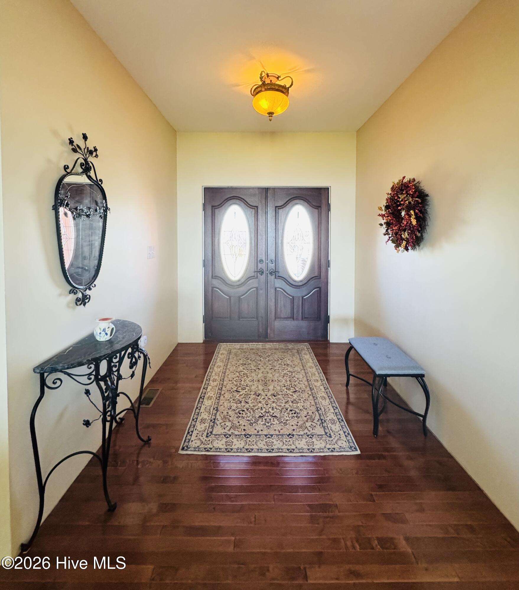 Entry foyer with dark wood double doors, hardwood floors, and a patterned runner.