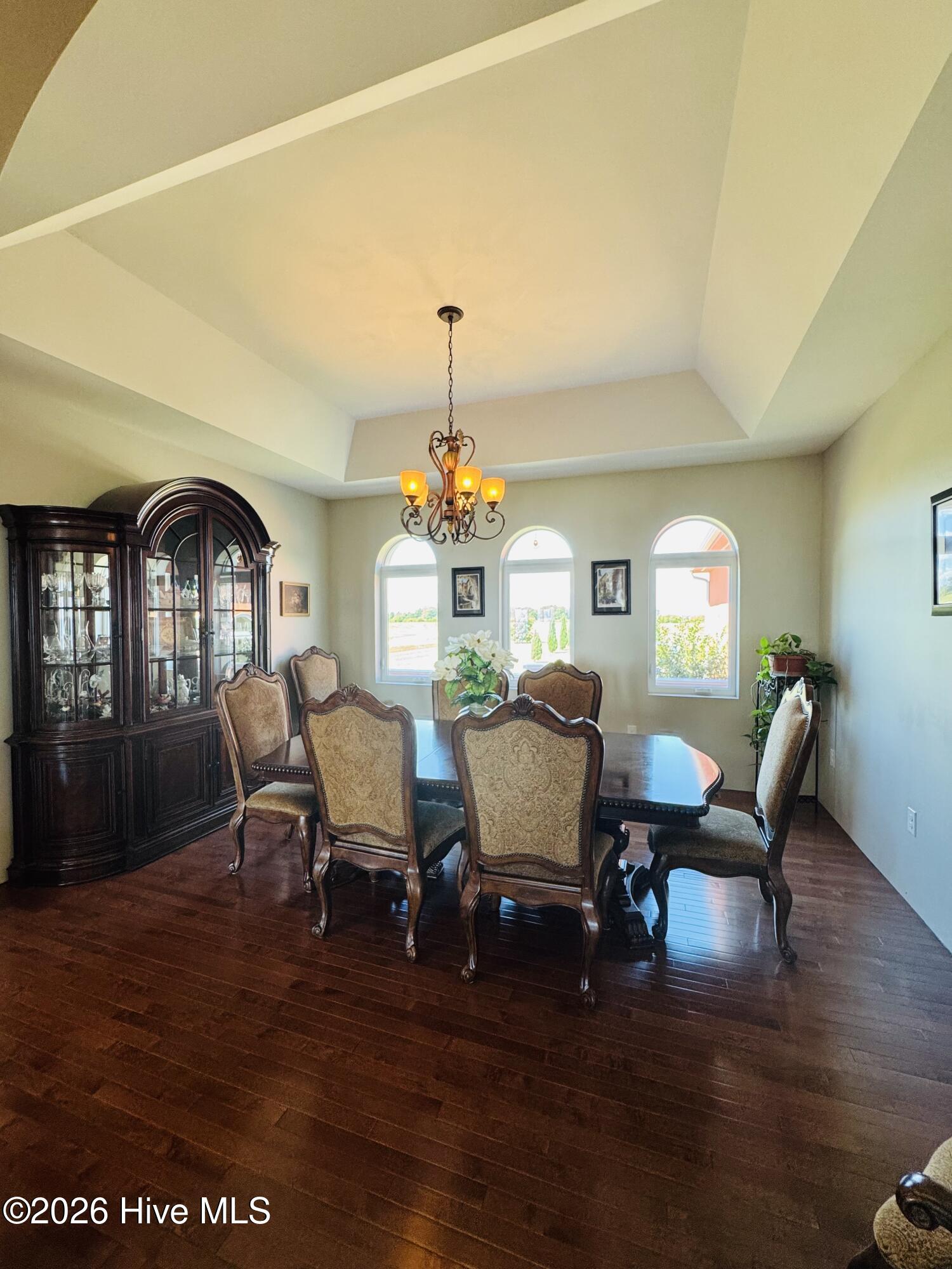 Dining room with a tray ceiling, chandelier, dark wood table, and three arched windows.