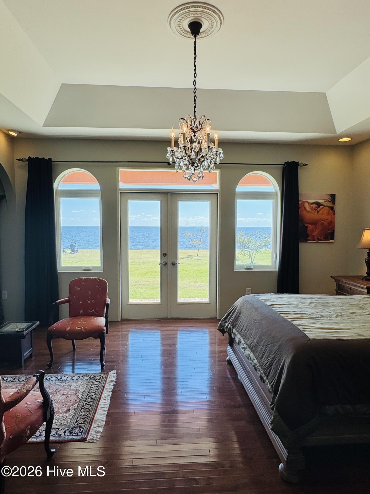 Bedroom with a crystal chandelier and French doors overlooking the water.