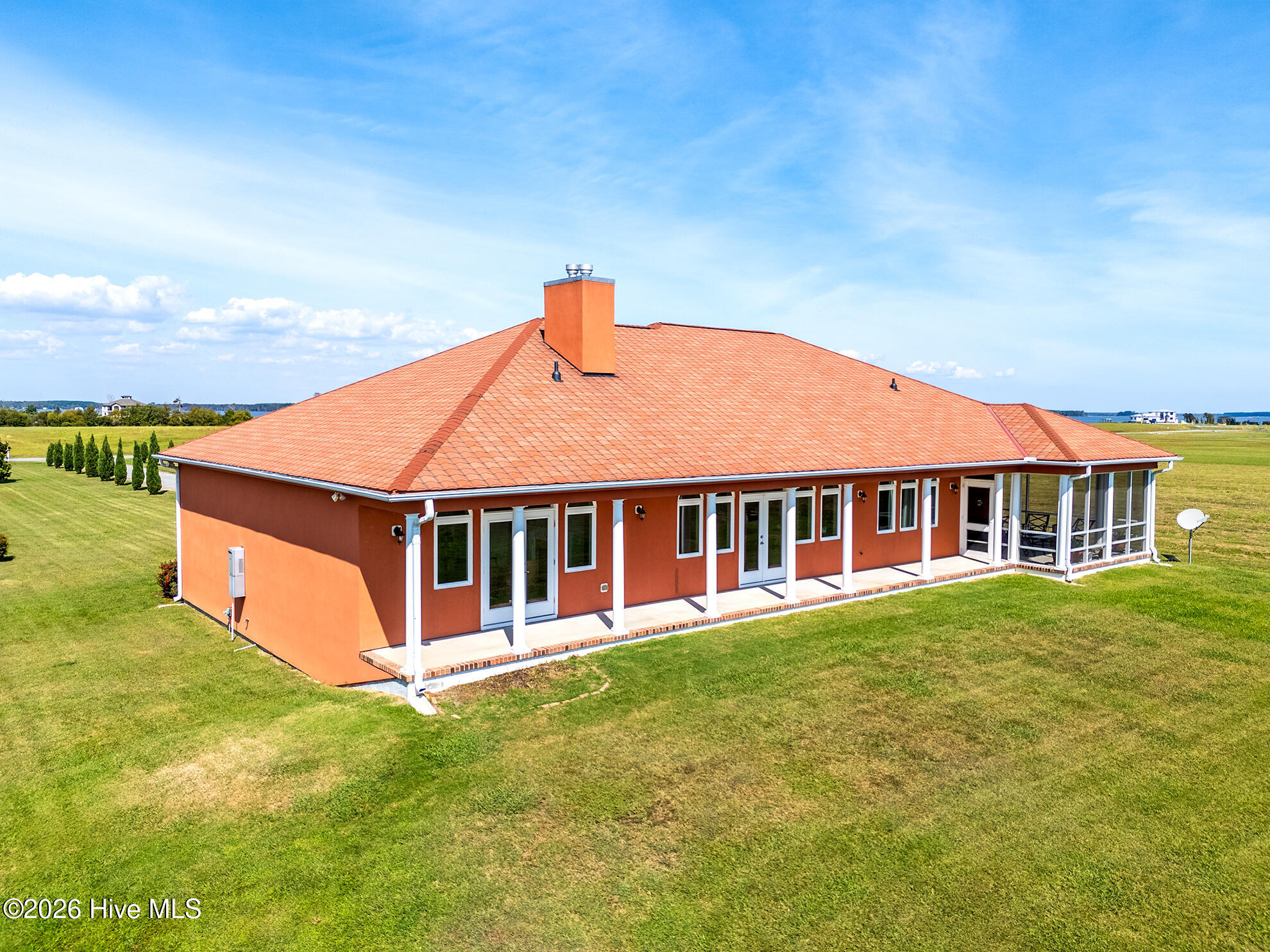 Orange house with a terracotta tile roof, long covered porch, and screened porch on an open lawn.