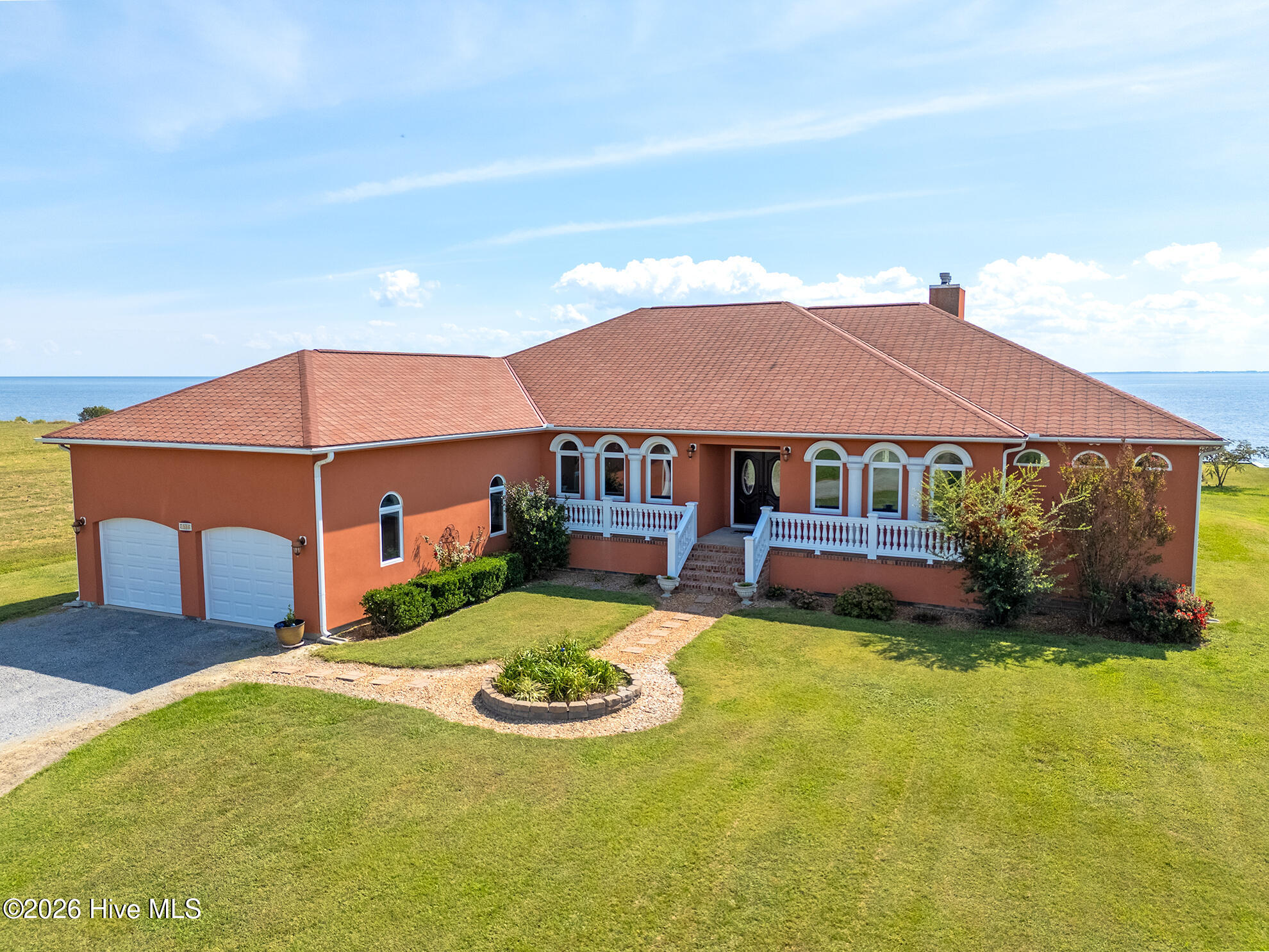 Terracotta waterfront house with arched windows, red tiled roof, and two-car garage beside a broad lawn.