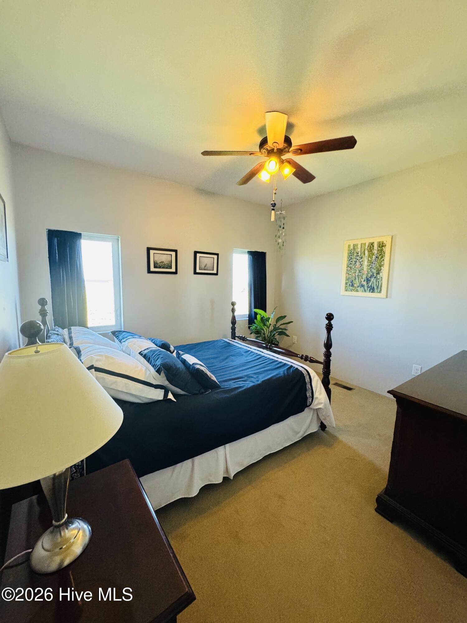 Furnished bedroom with a dark four-poster bed, blue bedding, and a lit ceiling fan.