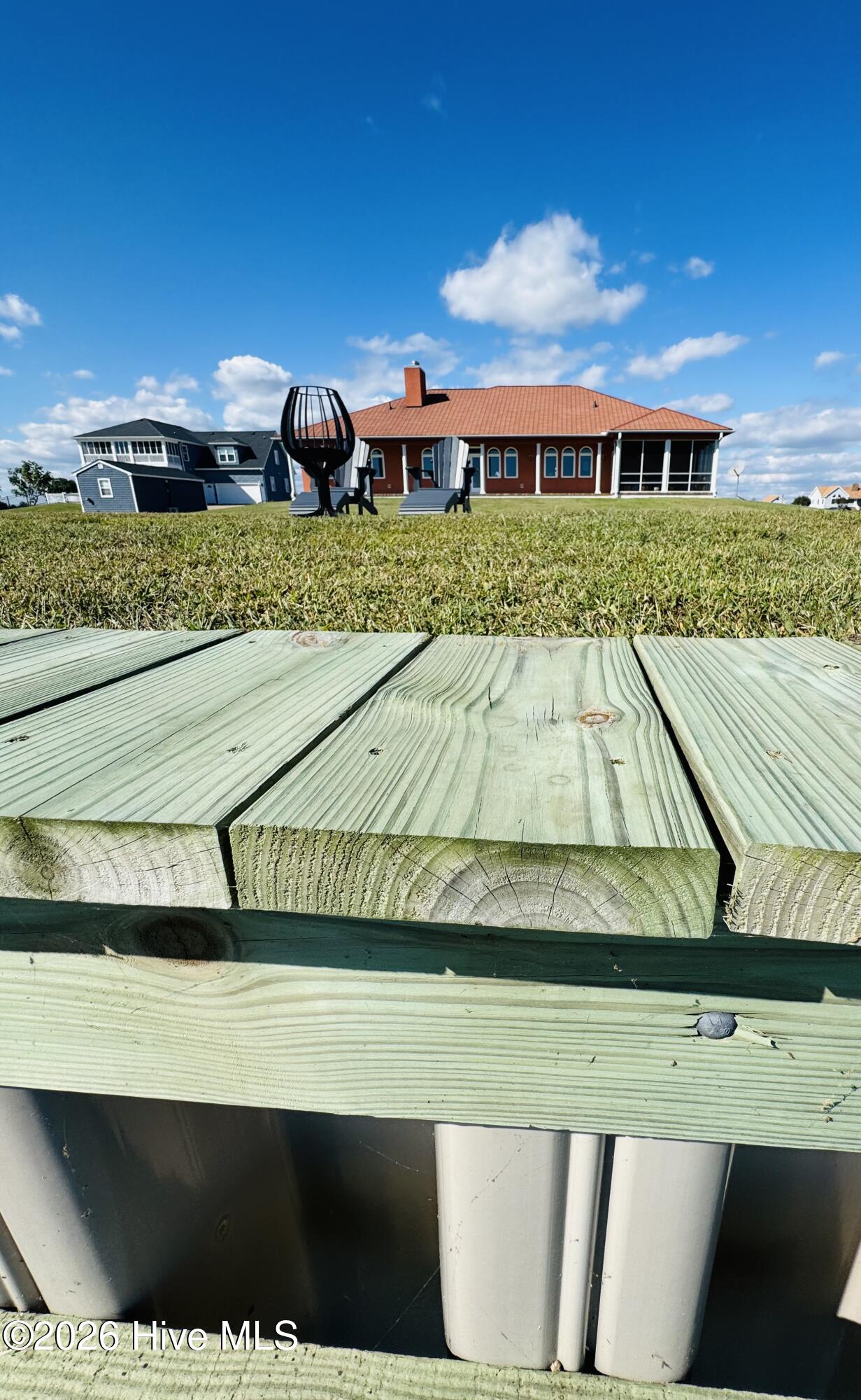 Red-roofed home beyond a grassy lawn, viewed from a raised wooden deck.