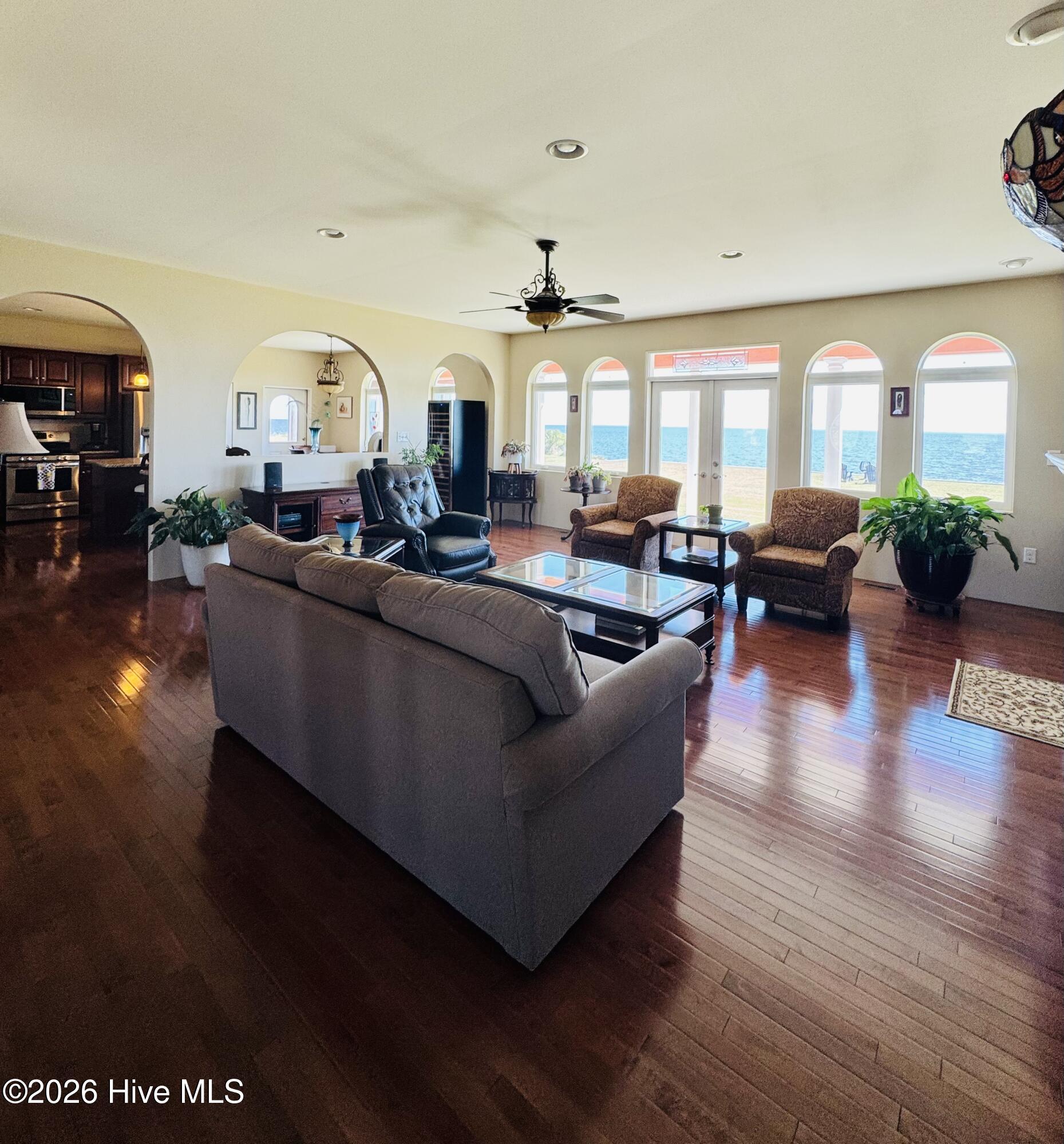 Living room with arched water-view windows, a gray sectional sofa, and glossy wood floors.