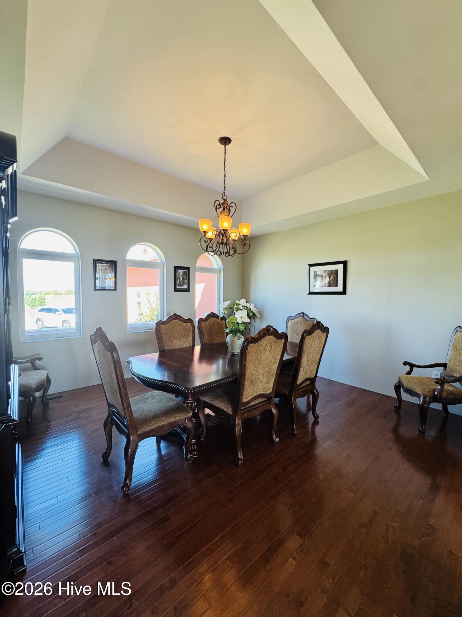 Dining room with a dark wood table, upholstered chairs, chandelier, and arched windows.