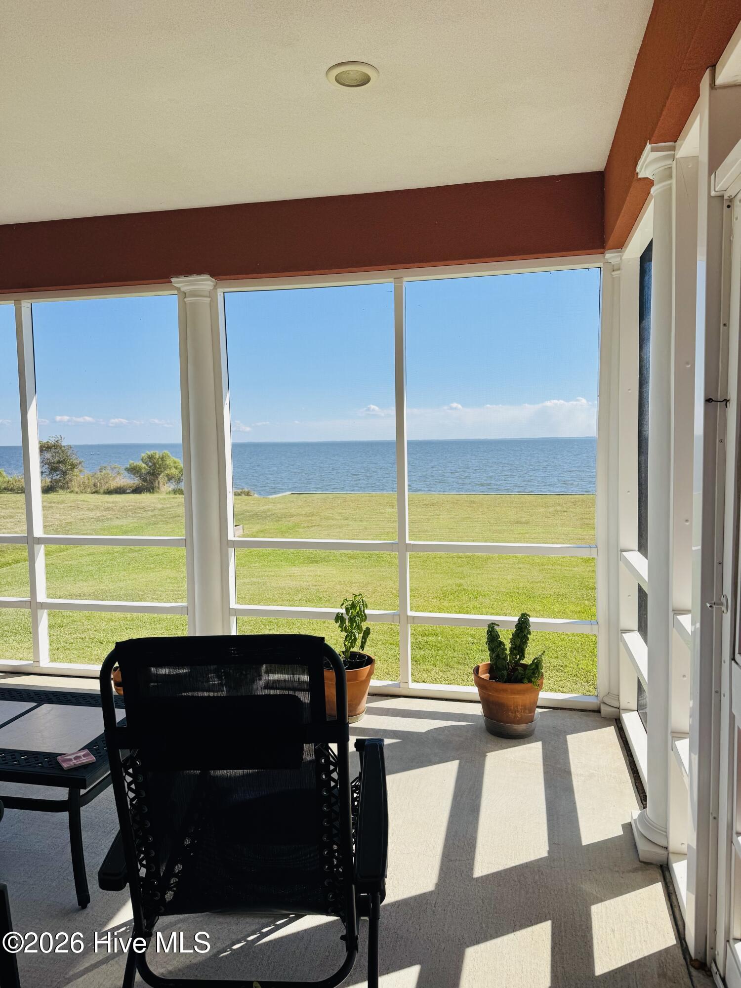 Screened porch overlooking the water, with white columns, potted plants, and a black chair.