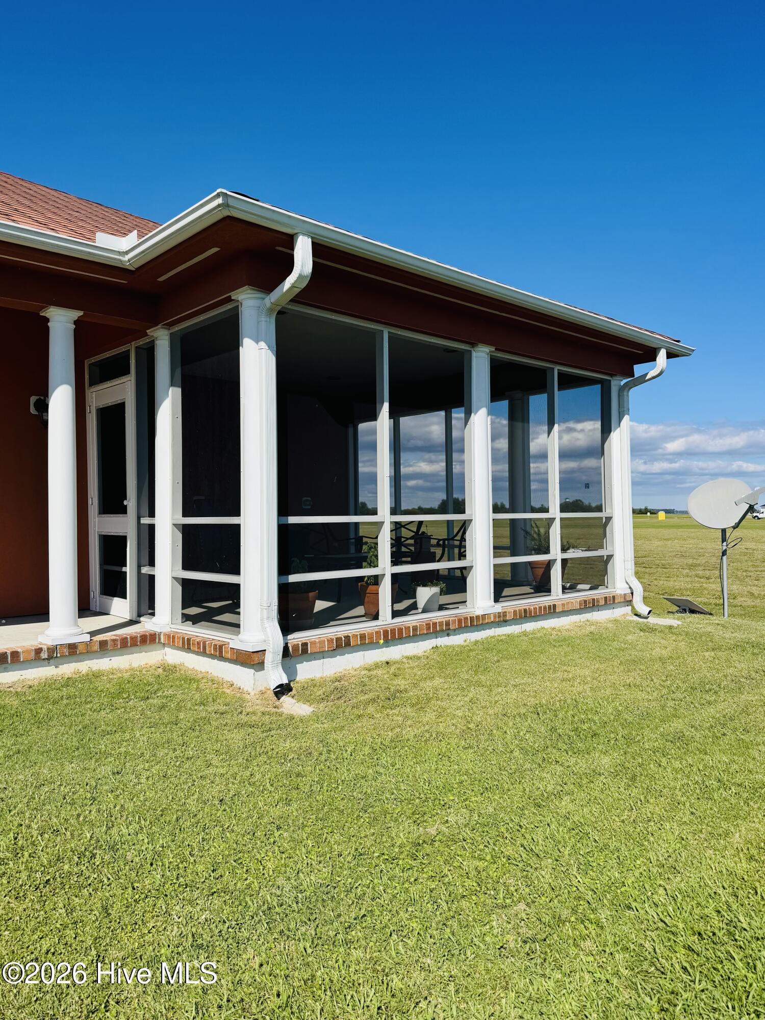Screened porch with white framing and brick edging beside a broad green lawn.