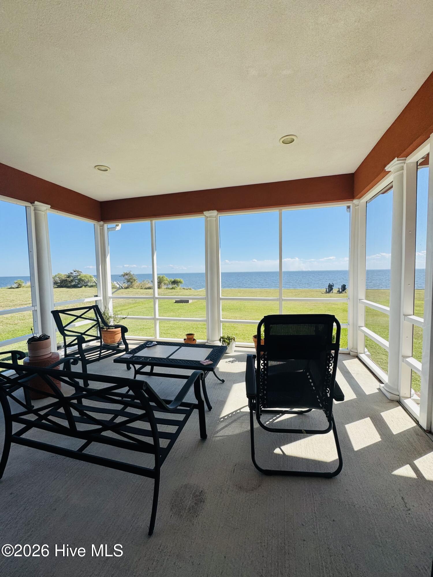 Furnished covered porch with black seating overlooking a grassy lawn and the water.
