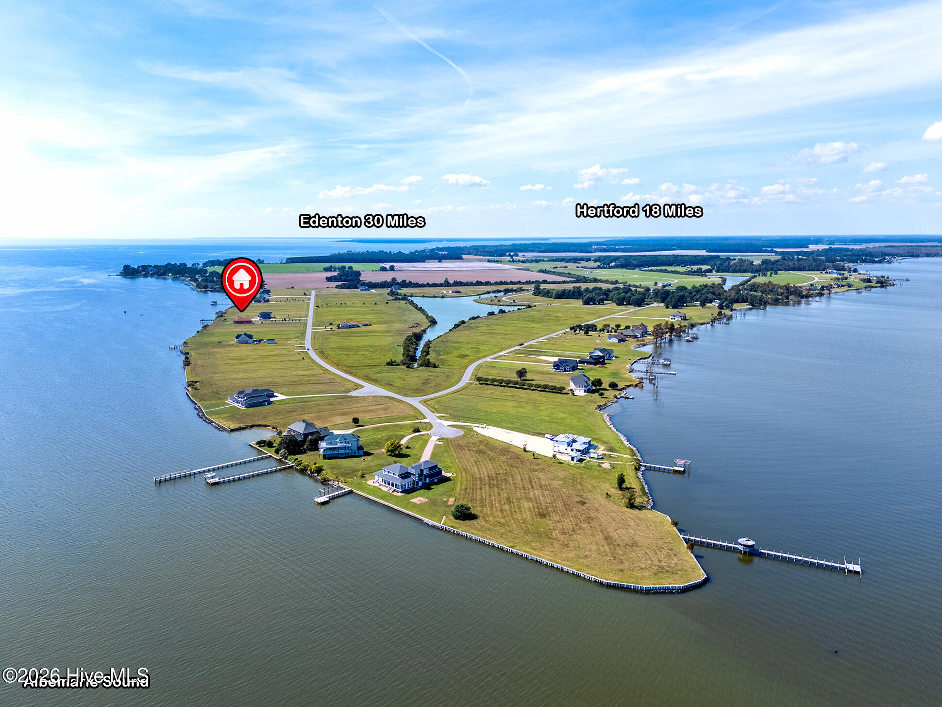 Aerial view of a waterfront peninsula with scattered homes, docks, and a red location marker.