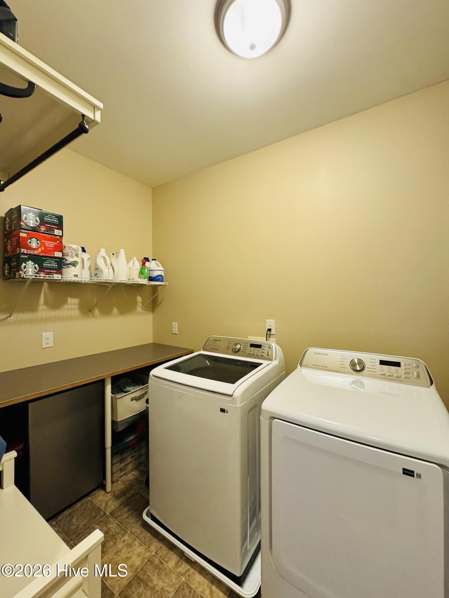 Laundry room with a top-loading washer, front-loading dryer, folding counter, and supply shelf.