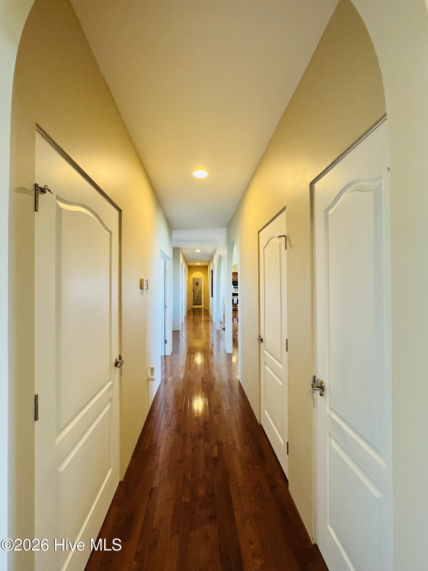Long hallway with polished wood floors, white paneled doors, and arched openings.