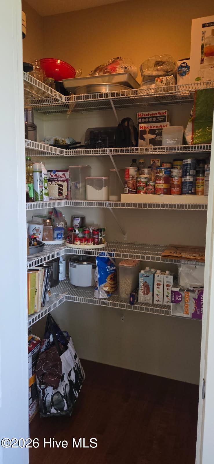 Walk-in pantry with stocked wire shelves and dark wood flooring.