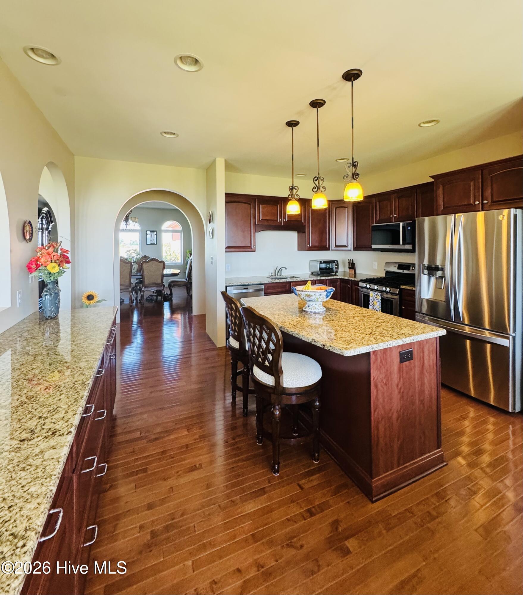 Kitchen with cherry cabinets, granite island, stainless steel appliances, and an arched opening to the dining room.