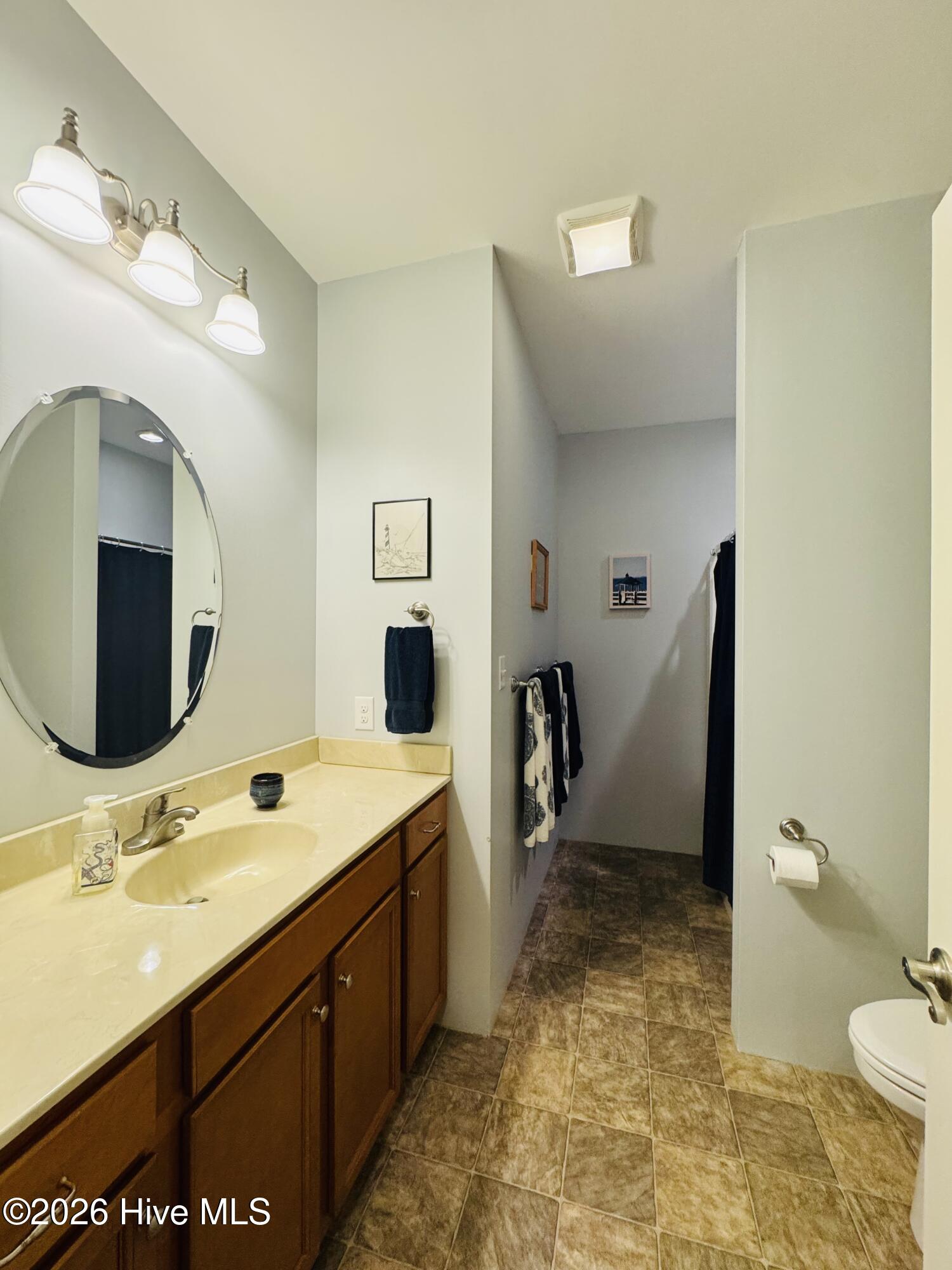 Bathroom with a long wood vanity, oval mirror, tiled floor, and partially visible toilet.