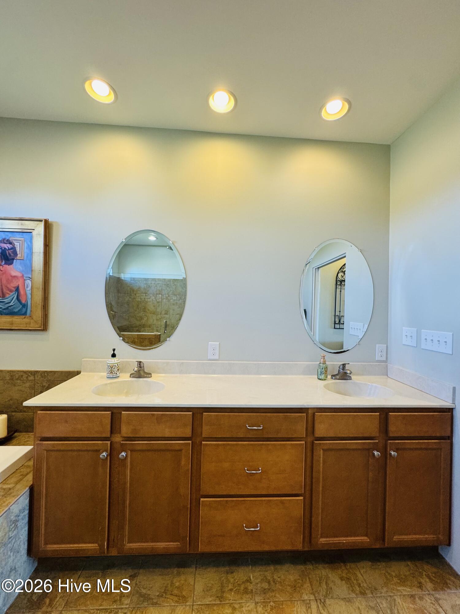 Bathroom with a wood double vanity, white countertop, and two oval mirrors.