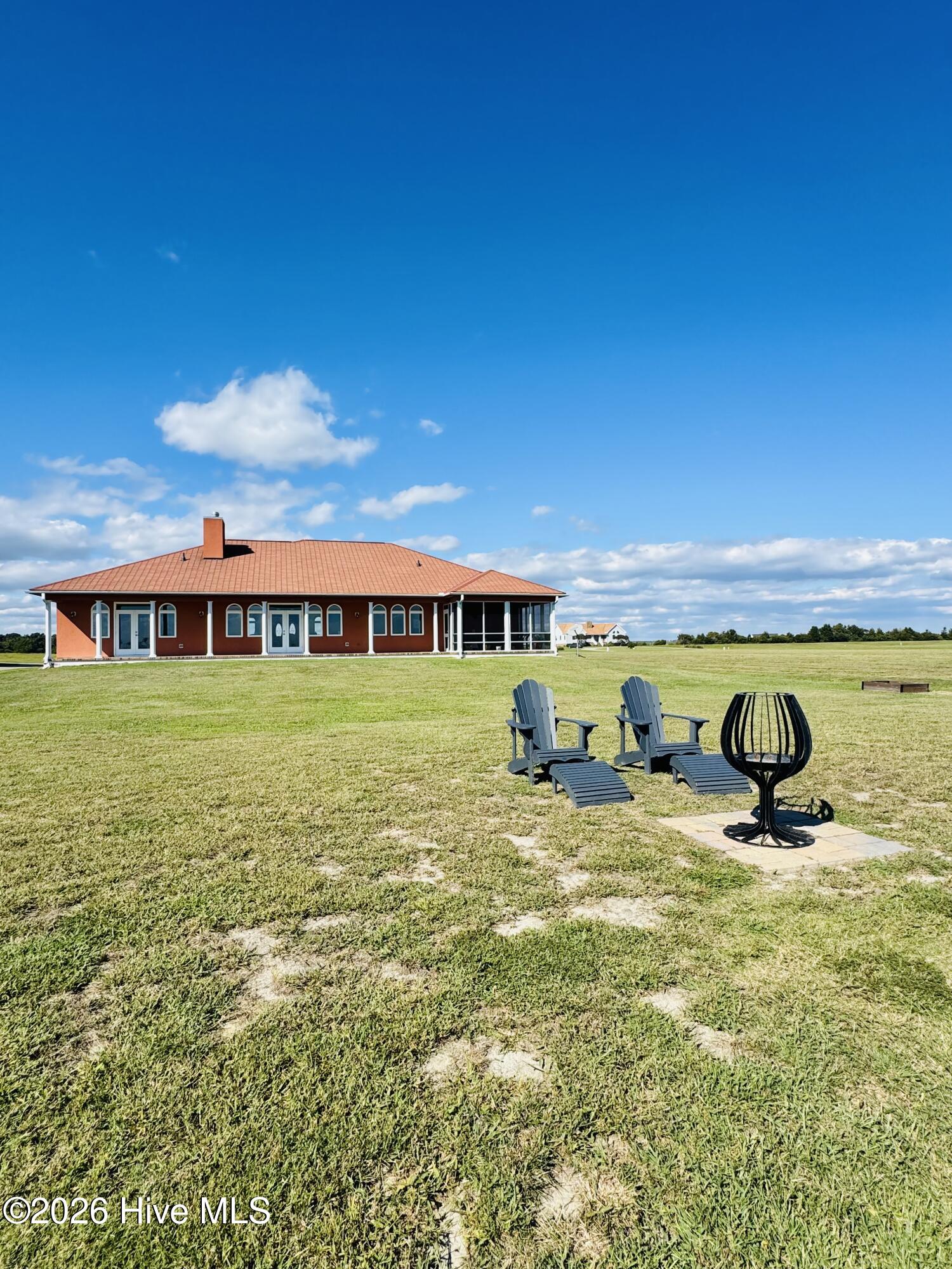 Red single-story home with a screened porch, broad lawn, Adirondack chairs, and a fire pit.