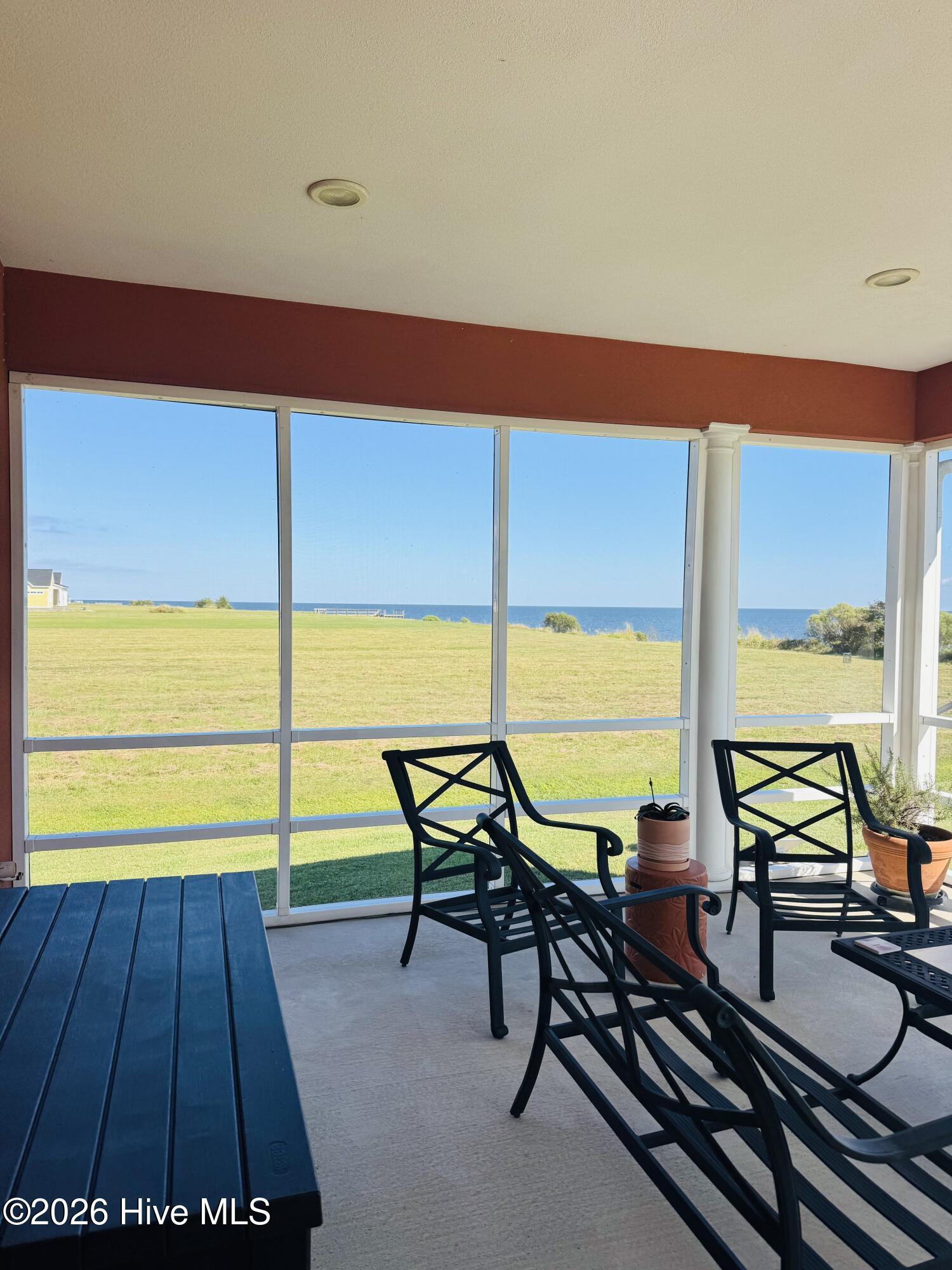 Covered porch with black chairs and ocean views across a grassy lawn.