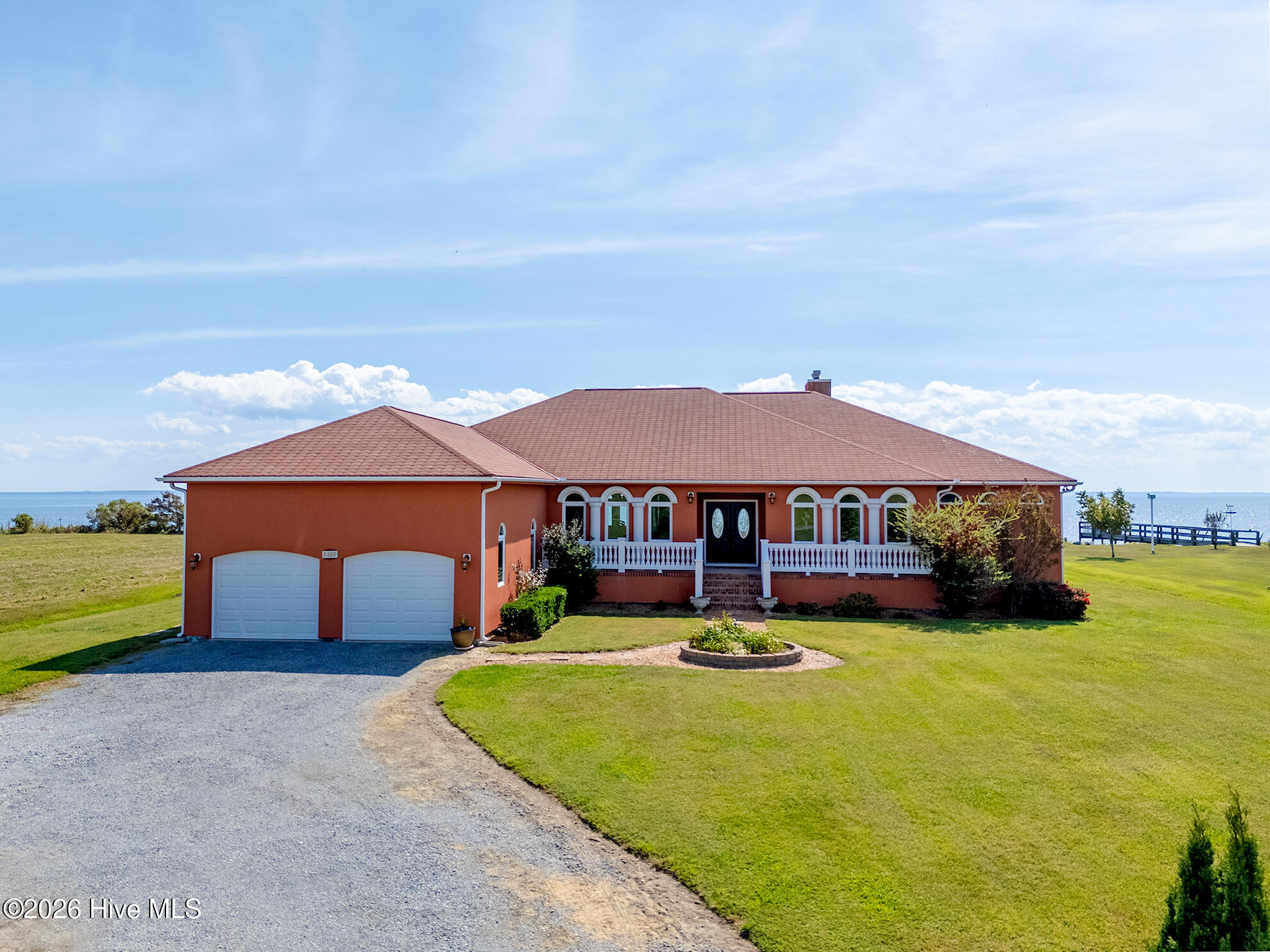 Red-orange waterfront house with arched windows, a double garage, and a broad lawn.