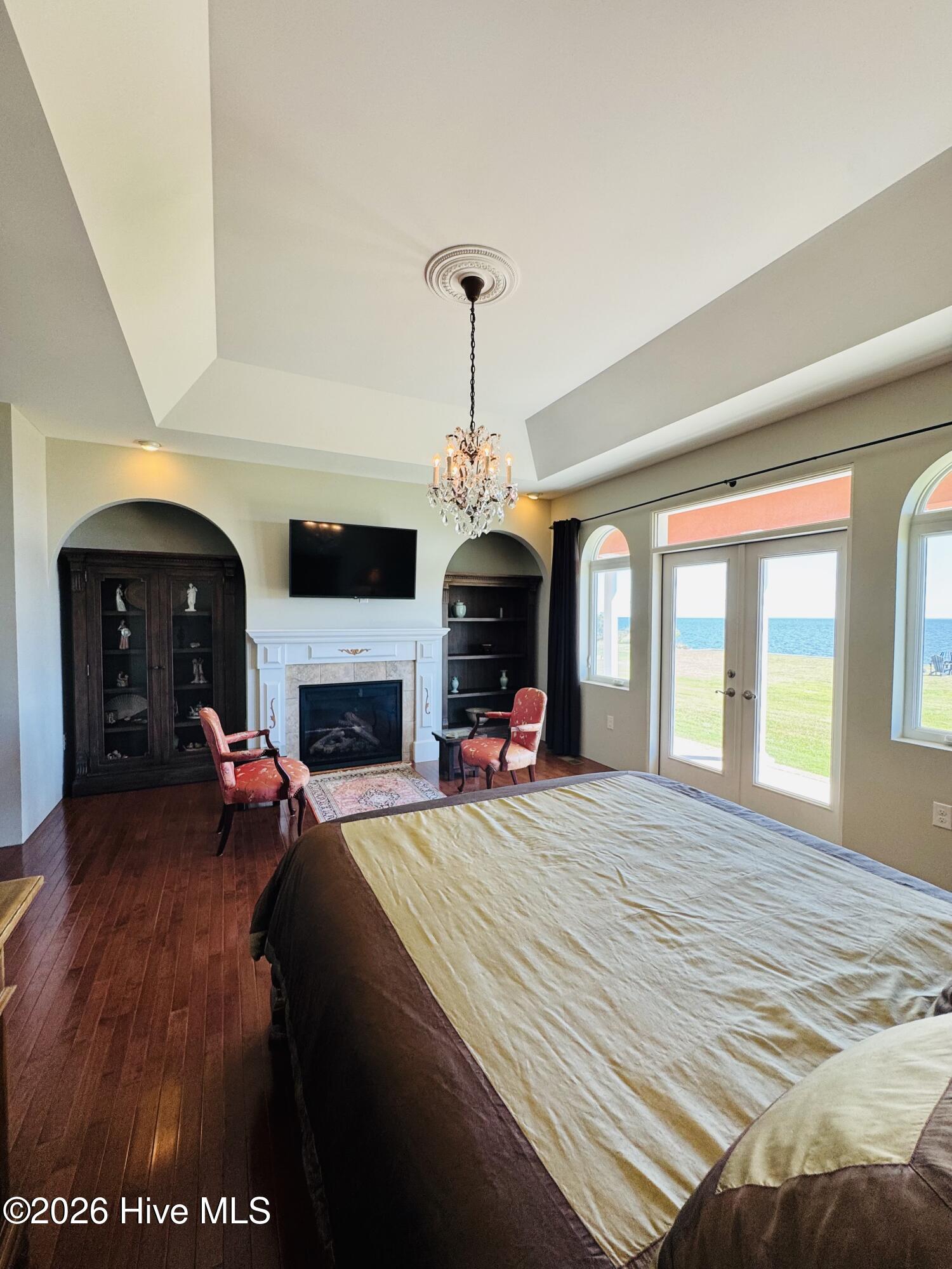 Bedroom with a fireplace, chandelier, and glass doors overlooking the water.