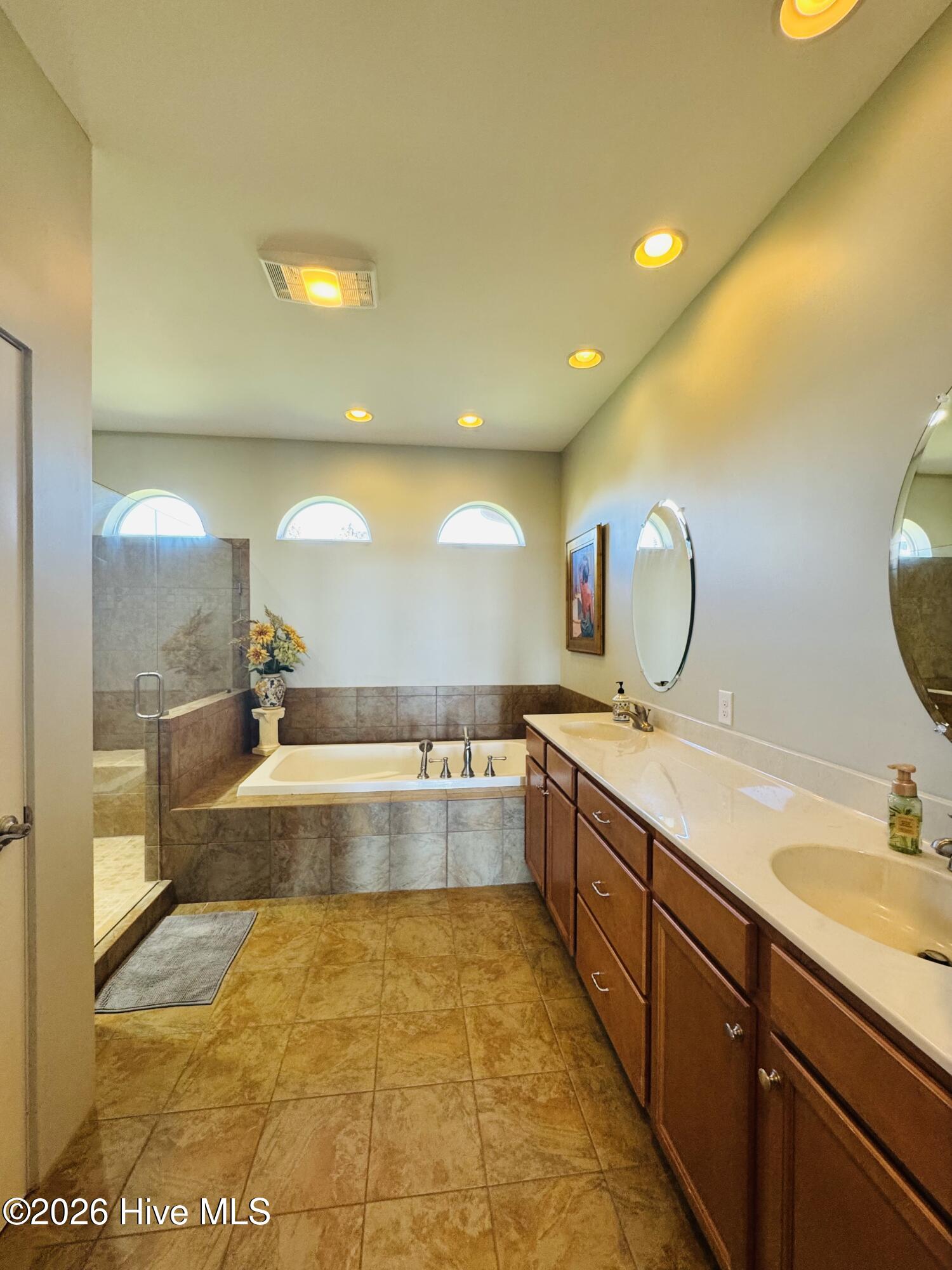 Bathroom with tiled walk-in shower, soaking tub, and long double vanity beneath arched windows.
