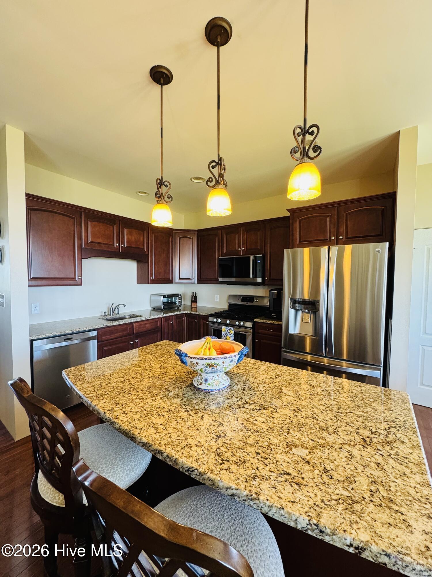Kitchen with dark wood cabinets, stainless steel appliances, and a large granite island.