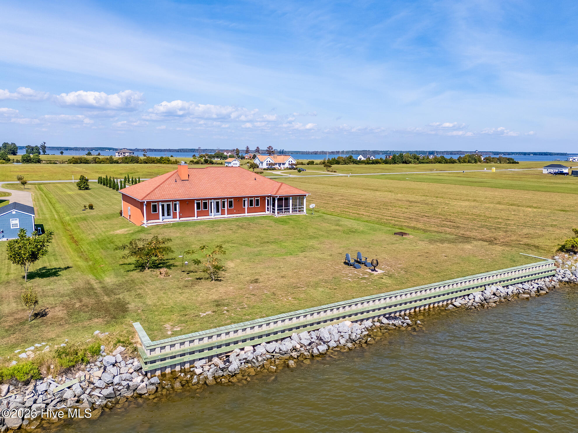 Waterfront home with a red tile roof, broad lawn, and long rock-armored seawall.