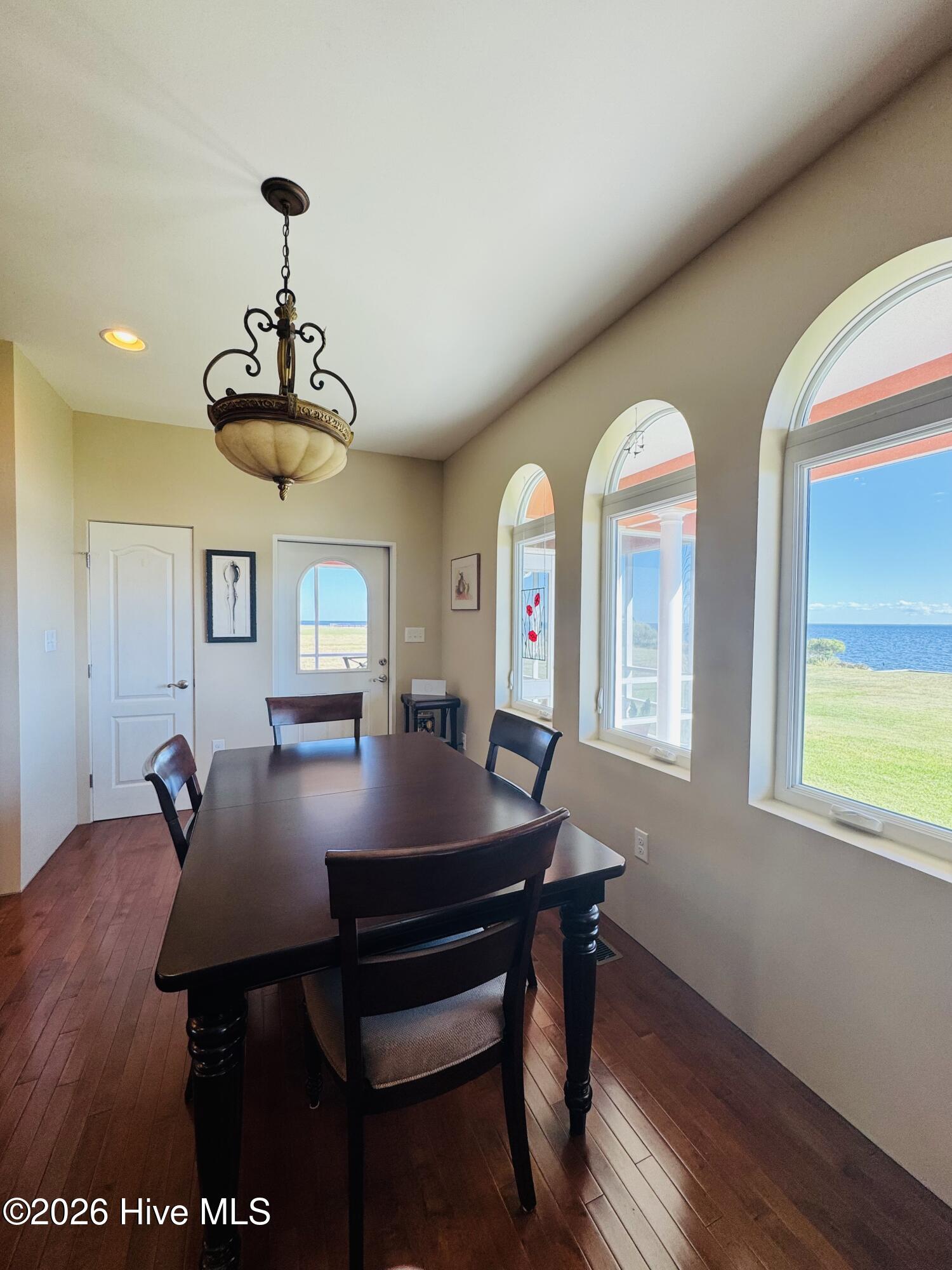 Dining room with arched windows overlooking the water and a dark wood table.