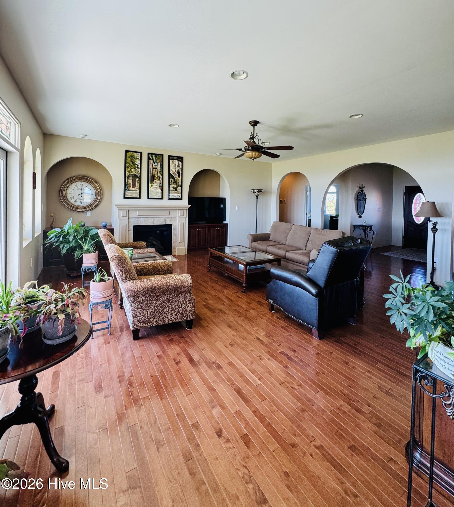 Furnished living room with hardwood floors, fireplace, arched openings, and ceiling fan.